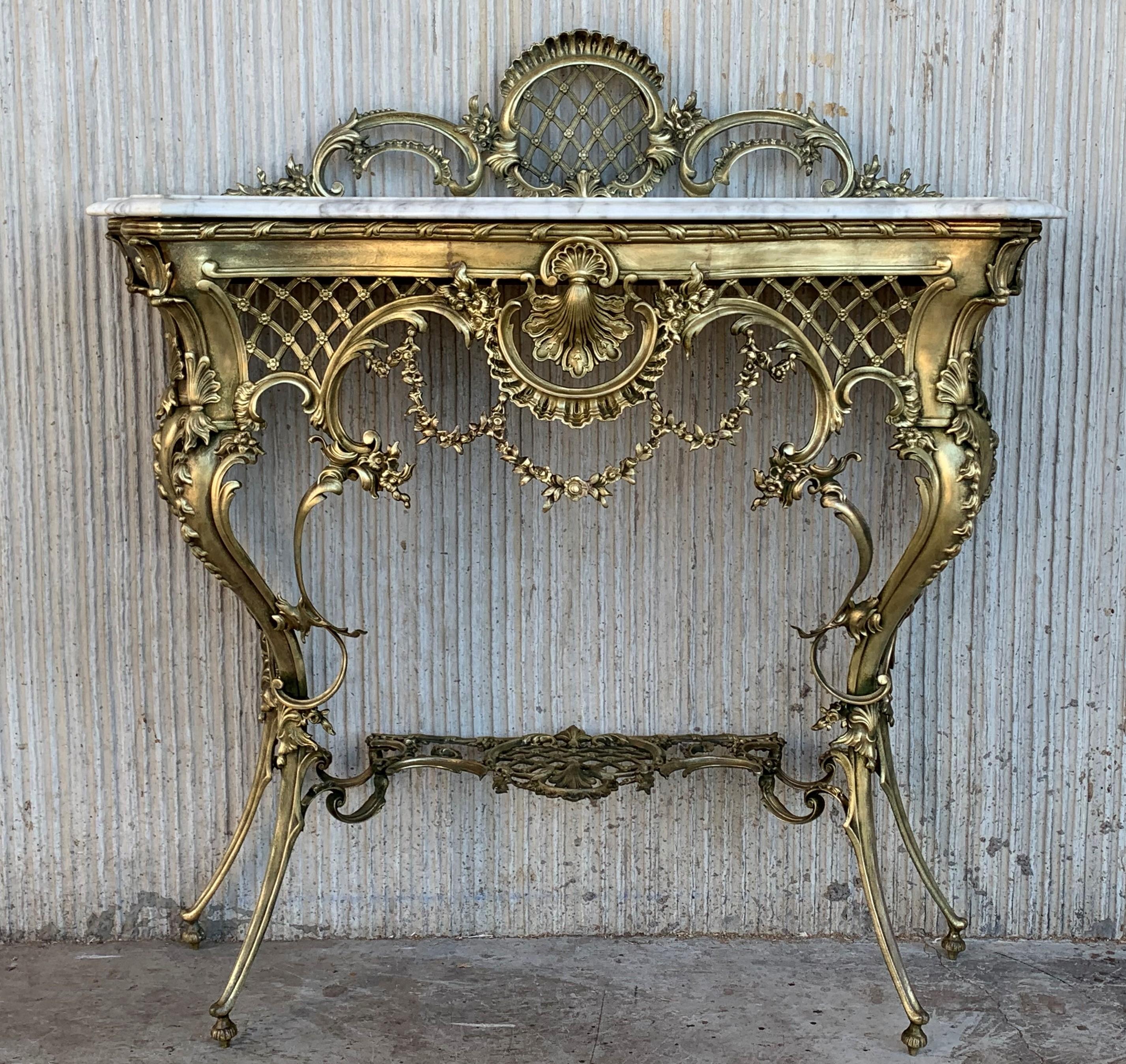 The white matble top with rounded corners mounted with an oval foliate decorated swivel bronze surmounted by a floral wreath and ribbon knot, raised on reeded legs joined by an interlaced stretcher and ending in toupie feet.
The console has a