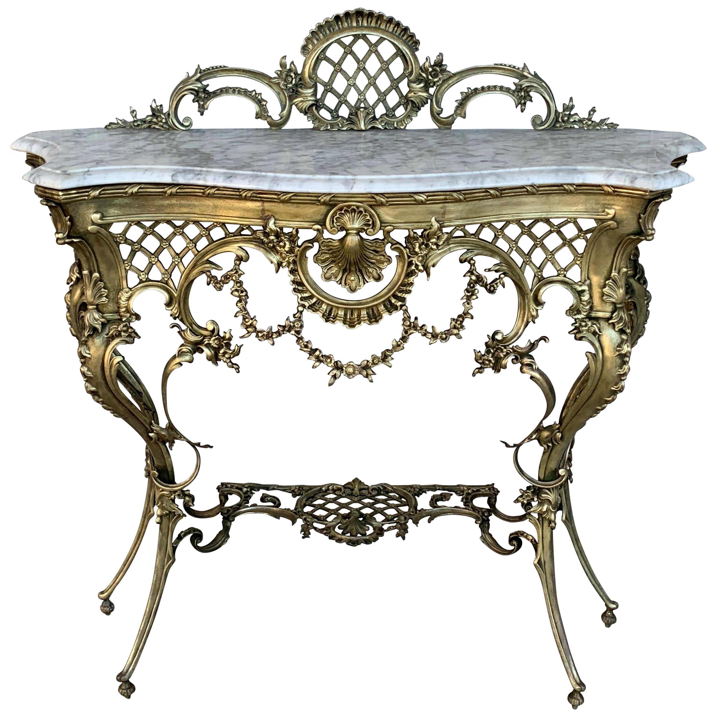 The white matble top with rounded corners mounted with an oval foliate decorated swivel bronze surmounted by a floral wreath and ribbon knot, raised on reeded legs joined by an interlaced stretcher and ending in toupie feet.
The console has a