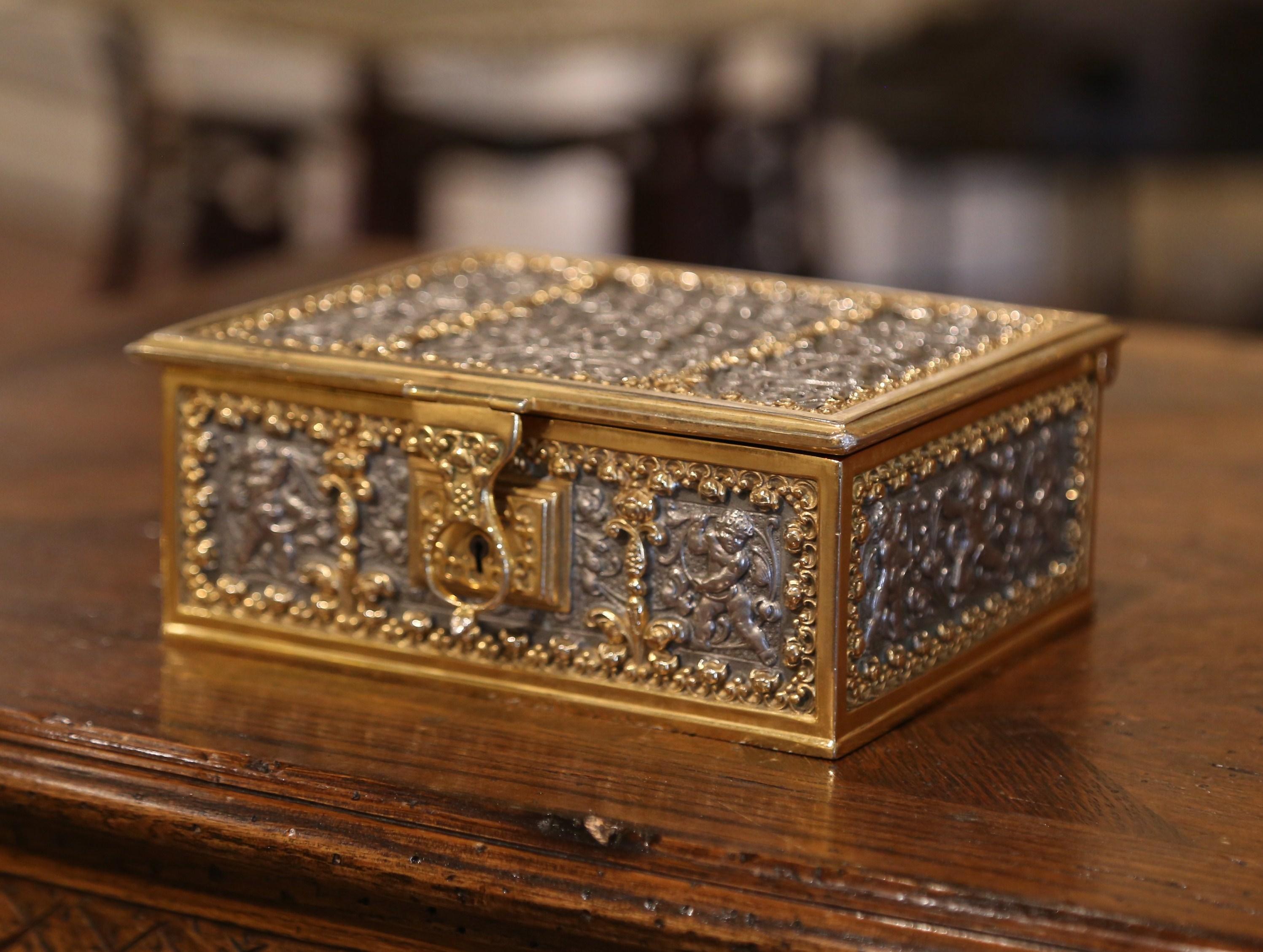 This antique two-tone casket was created in France, circa 1880. Rectangular in shape, the gilt bronze and pewter box is embellished with cherub and scroll motifs. The detail work is outstanding with bas relief decor on all five sides. The inside box