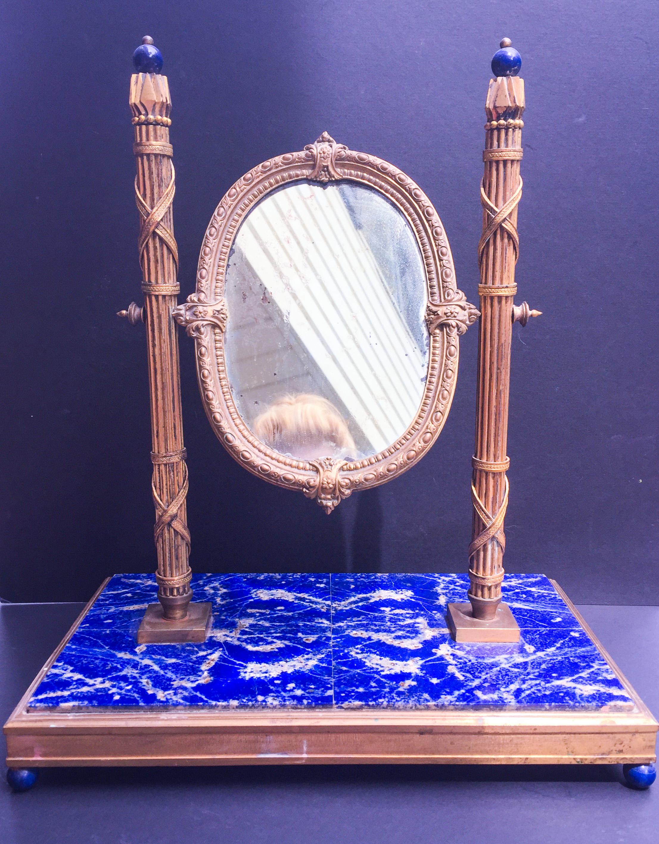 This French, 19th century mirror with ormolu bronze Roman Fasces Columns is created in the Empire style. It is mounted on a large rectangular base of solid and strongly colored Lapis Lazuli. It is surrounded with a gilded bronze band and stands on