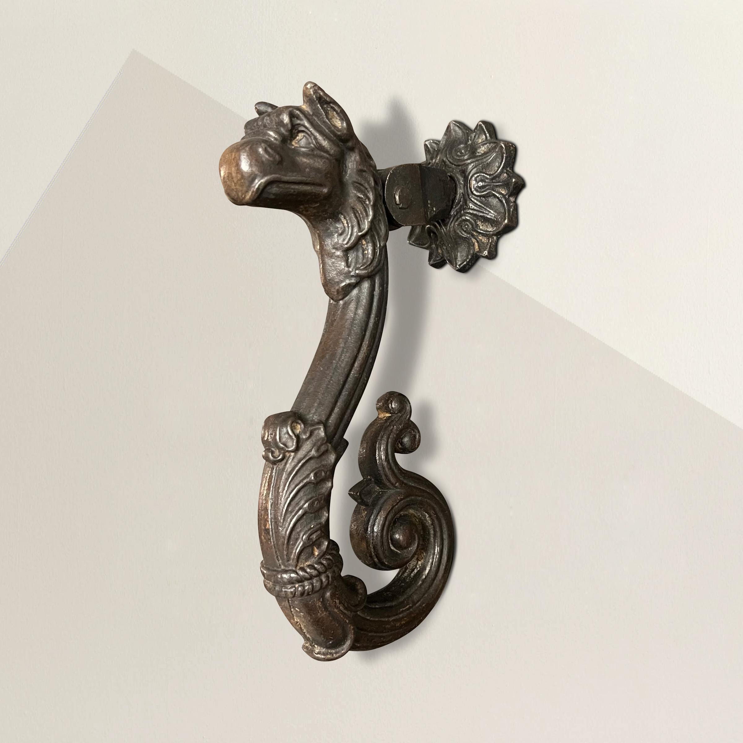 A stunning 19th century French cast bronze door knocker with a griffin head over a scrolled body with foliate details, and backed with a floral roundel backplate.