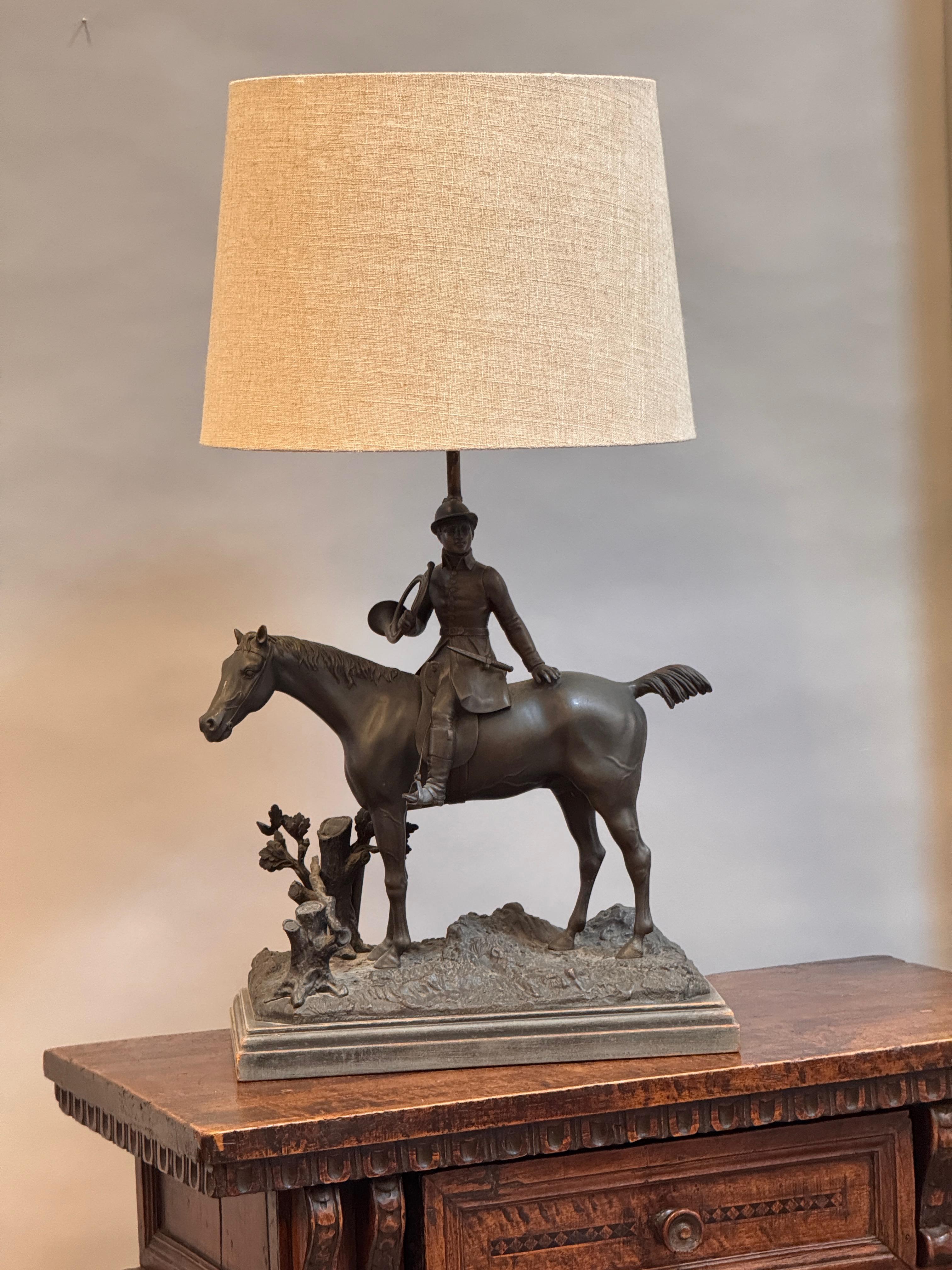 Cast bronze figural lamp base depicting a mounted huntsman, with a coiled hunting horn over his shoulder. Richly detailed throughout— from the textured terrain base to the reins and saddle gear—this piece is late 19th century. A richly patinated