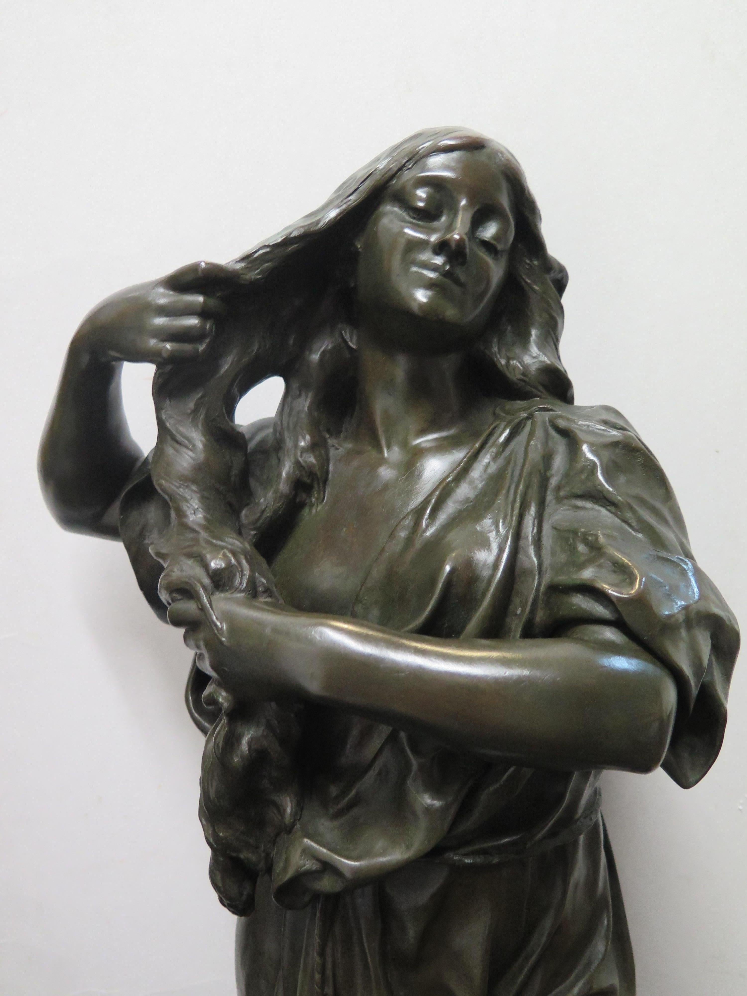 This stunning vintage late 19th century patinated bronze sculpture of a woman was created by Emile Peynot. The full figured “earthy” European woman in a loose fitting robe is positioned standing attempting to air dry her long hair. She is featured