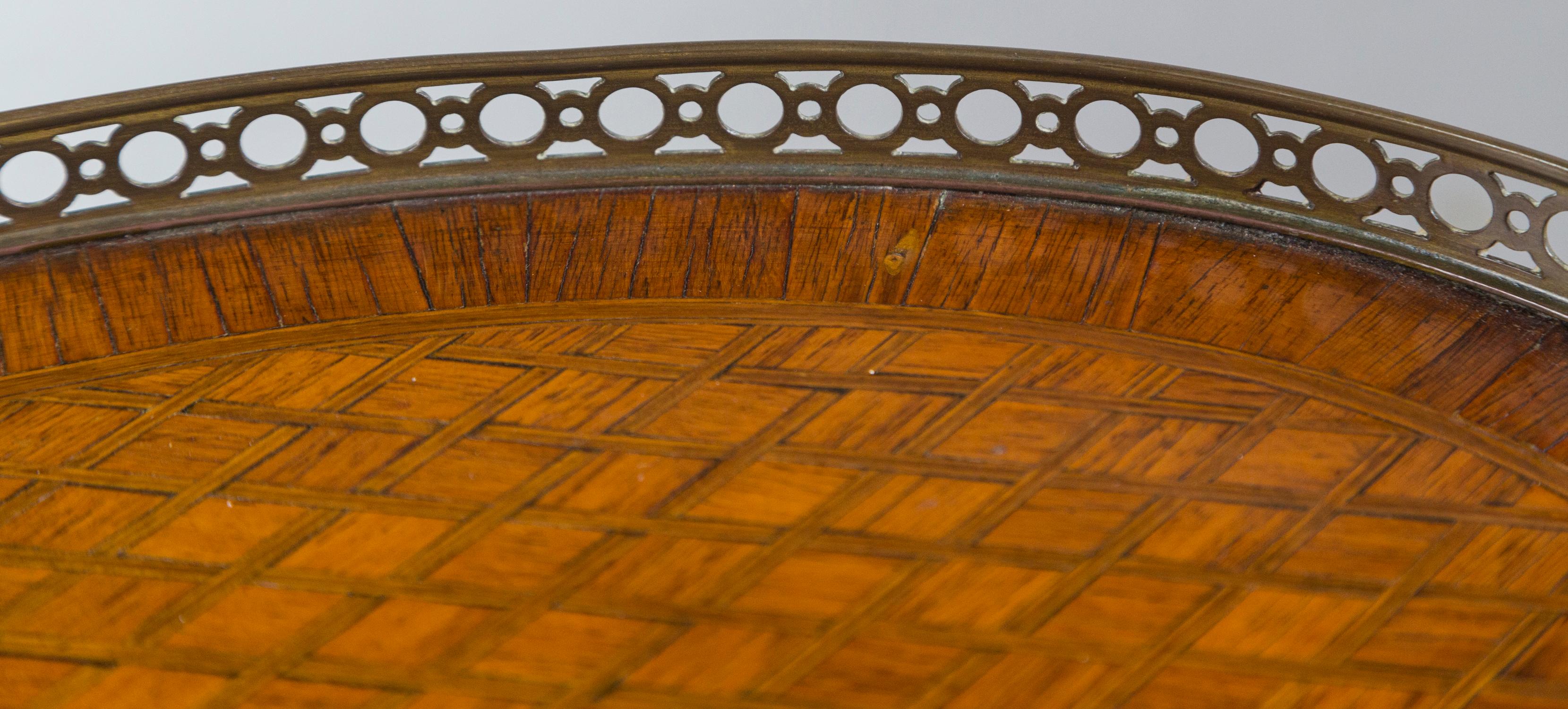 The top and the lower shelf inlayed in a geometric pattern with crossing lines of possible sycamore in the light mahogany. The apron and drawer front of the same inlays. A three quarter bronze gallery at the top with a bronze band on the lower