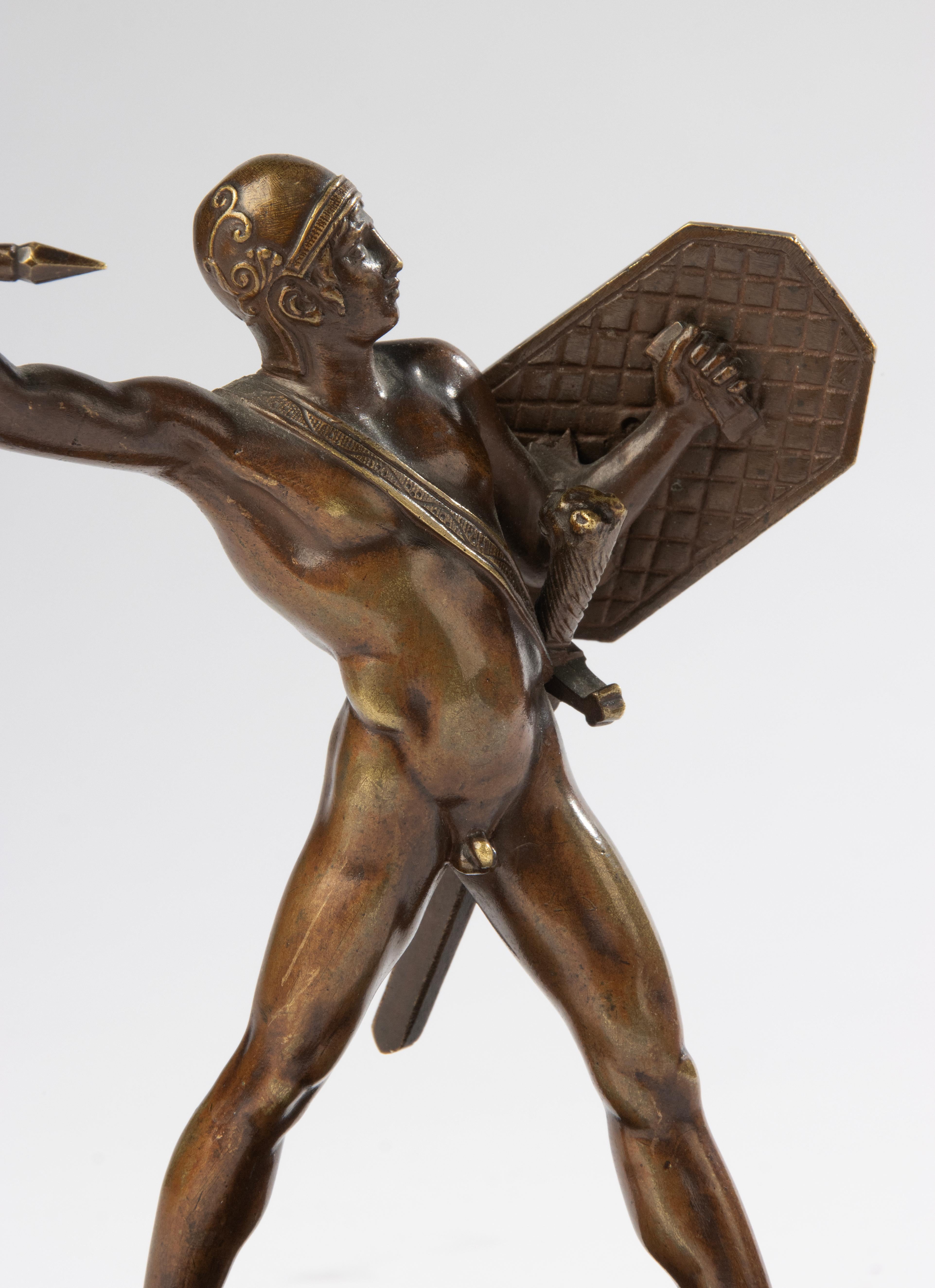Cette sculpture en bronze finement coulée, réalisée en France à la fin du XIXe siècle, est une représentation saisissante d'un guerrier grec classique - probablement un hoplite - pris dans le mouvement dynamique du lancement d'une lance, bouclier à