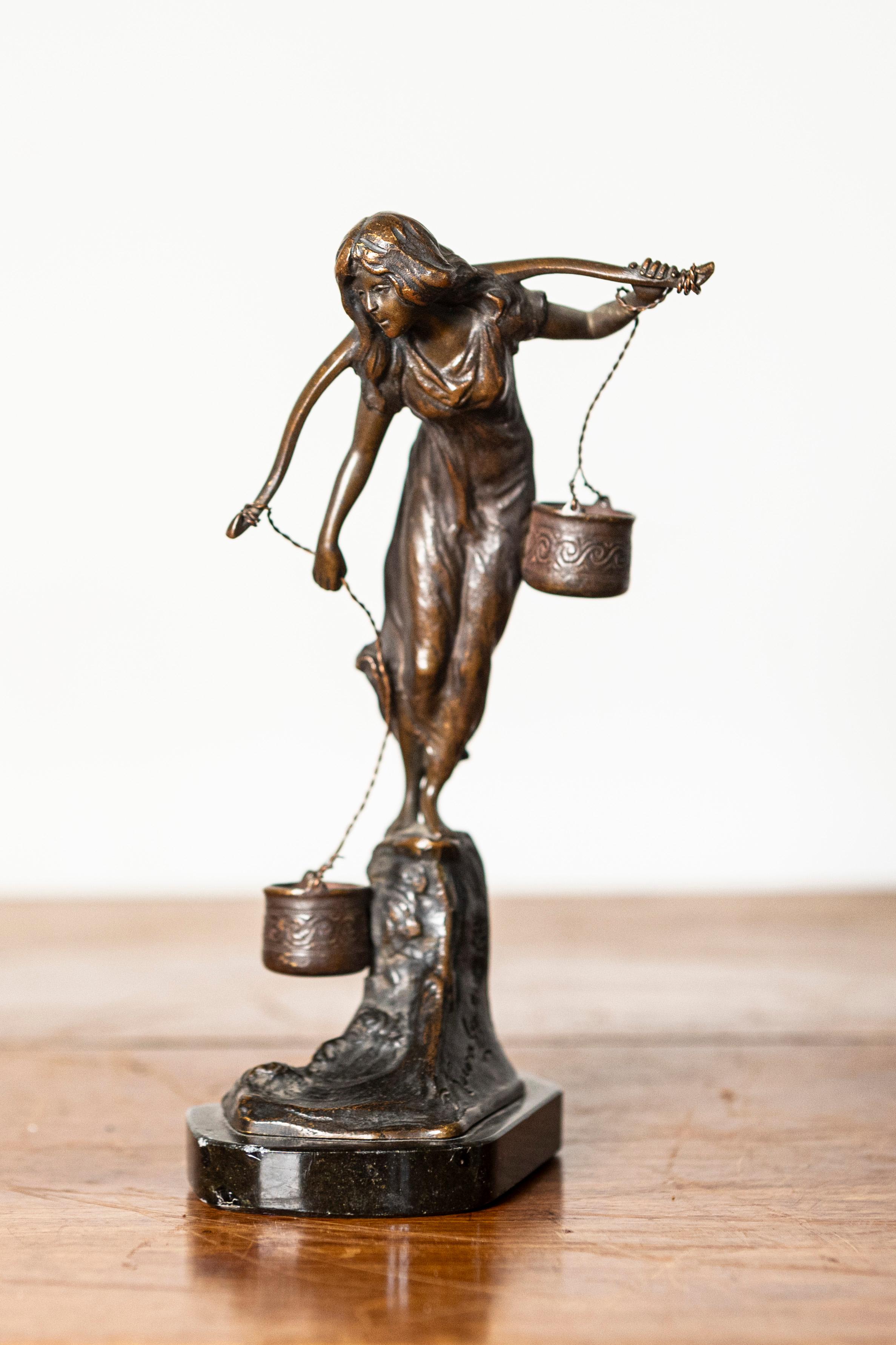 Questa raffinata scultura in bronzo francese del XIX secolo ritrae una giovane donna che bilancia con grazia due secchi d'acqua ornati e sospesi da un giogo sulle spalle. La meticolosa attenzione dell'artista per i dettagli è evidente nel panneggio