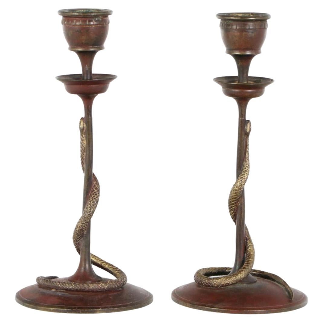 A pair of 19th century antique French gilded bronze candlestick holders. Orientalist design with slender stems surmounted by leveled candle pricket cups, and encircled by gilded dore bronze serpent forms, terminating upon red enameled circular