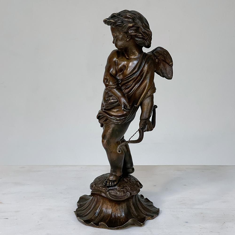 19th Century French bronze statue of cupid captures the mischievous cherub just after letting his arrow fly. The classic pose inspired by ancient Greek and Roman statuary is evident, with flowing scarf providing additional visual appeal as well as a