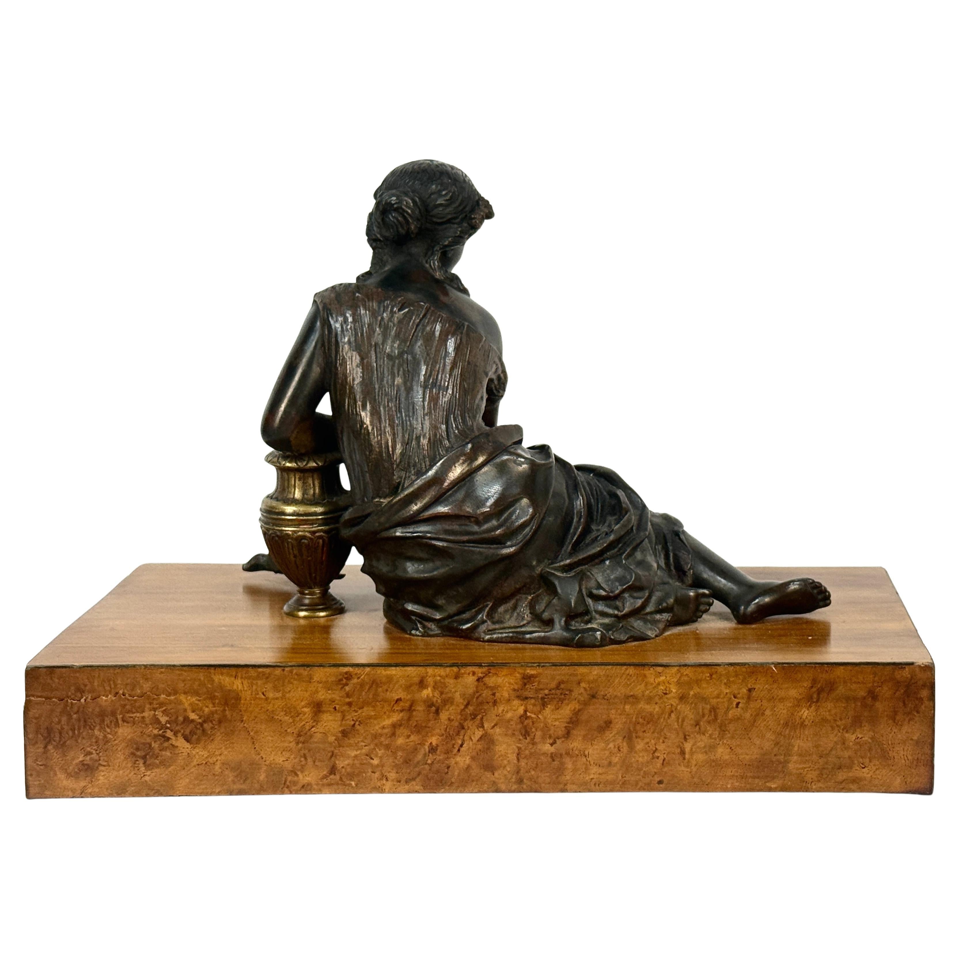 19th Century French Bronze Woman with flowing garments amid flowers and an urn. Flowers often represented beauty, life and the passage of time while urns are traditional symbols of memorial, love, or permanence. She rests on a large burl wood