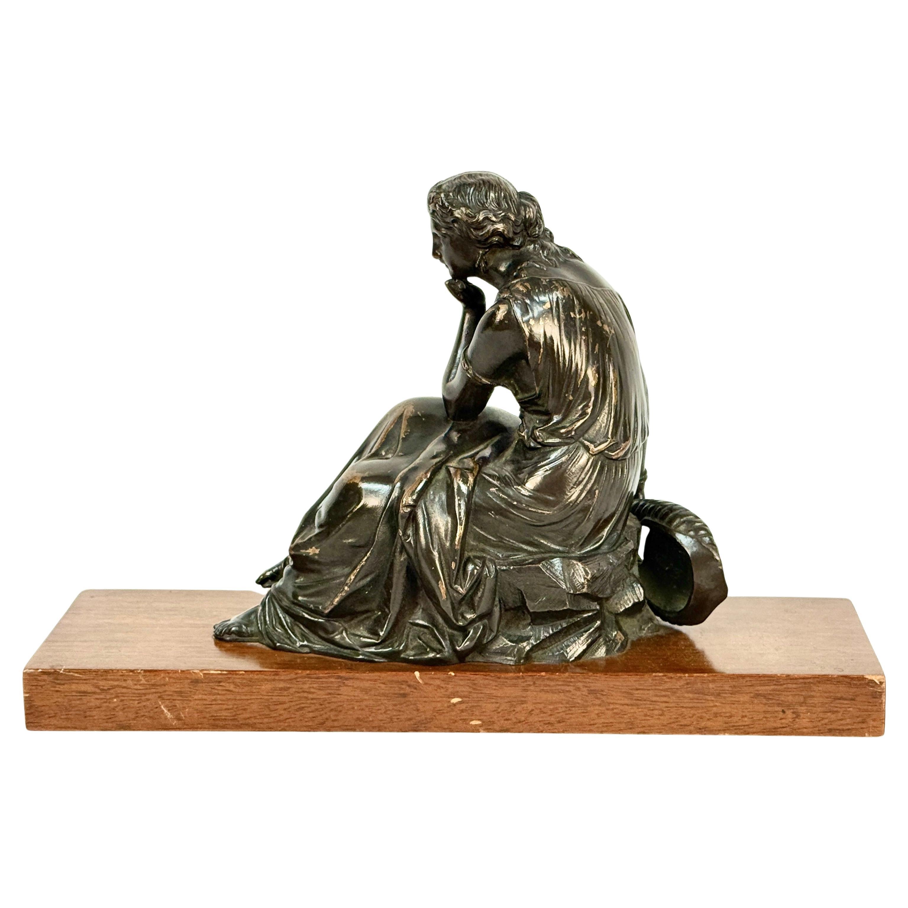 Bronzo francese del XIX secolo Donna seduta con il suo strumento a lira al fianco. È in posizione seduta con una mano sotto il mento come se stesse riflettendo su qualcosa. È vestita in modo elegante con abiti classici e con dettagli superbi su