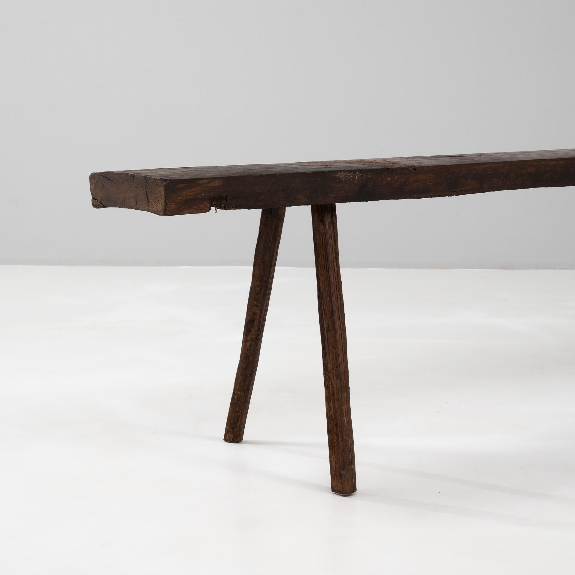 Ce banc en bois brutaliste français du XIXe siècle est un exemple d'artisanat brut et d'authenticité rustique. Taillée à la main dans du bois massif, elle présente une assise en planches épaisses et irrégulières soutenue par quatre pieds robustes à