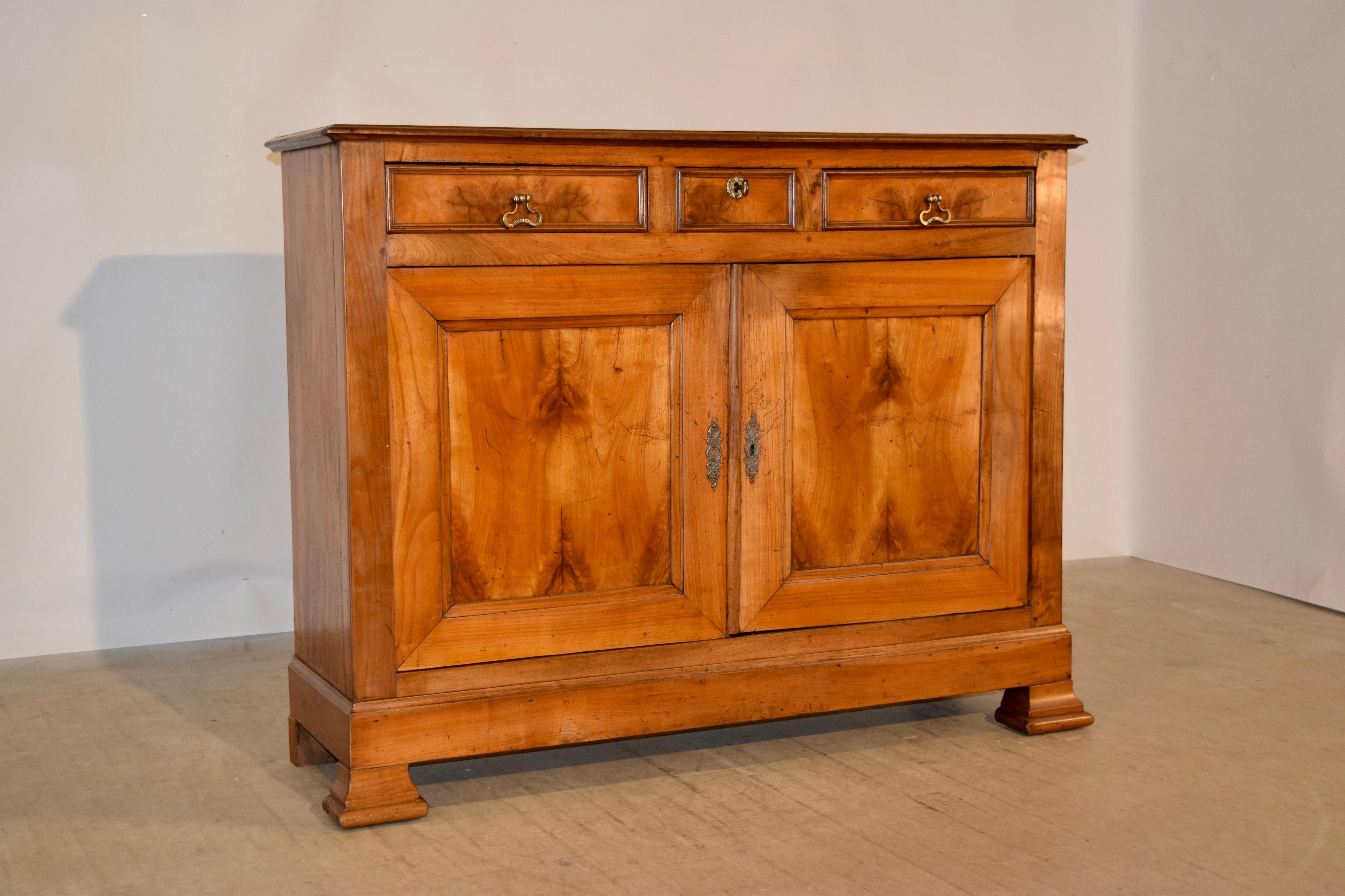 19th century, French buffet made from cherry with a banded top and a beveled edge over a small central drawer flanked by two drawers over two doors, which open to reveal storage. The sides are simple and have lovely graining. The piece is raised on