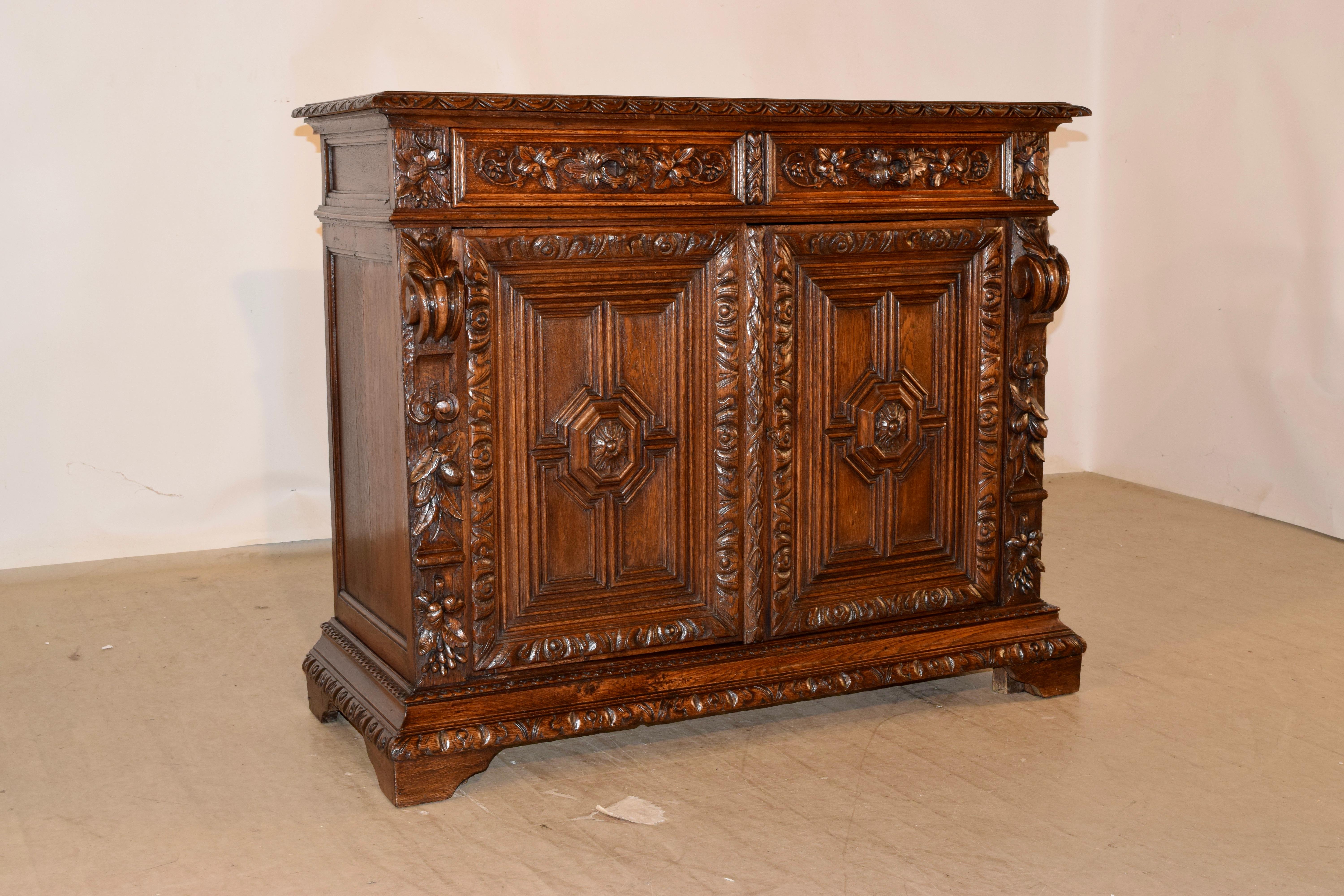 19th century oak buffet from France with a beautifully molded and hand carved lunette decorated edge around the top, following down to lovely and simple hand paneled sides and two drawers over two doors in the front, which open to reveal shelving.