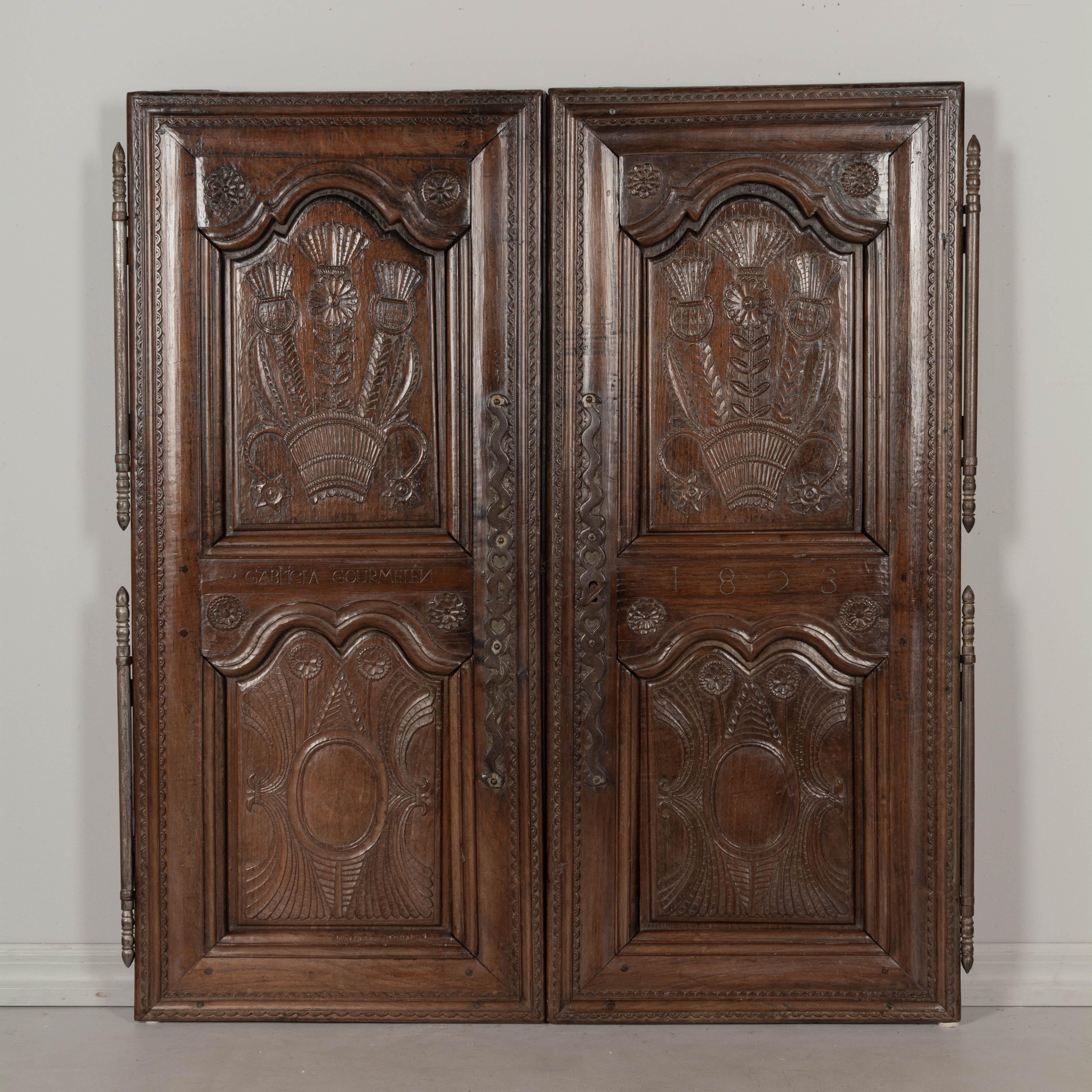 A set of early 19th century French doors from a cabinet or cupboard, crafted of solid chestnut. Thick panels with beautiful hand-carved stylized floral motif and waxed patina. Decorative cast iron escutcheons and large hinges. Working lock and key.