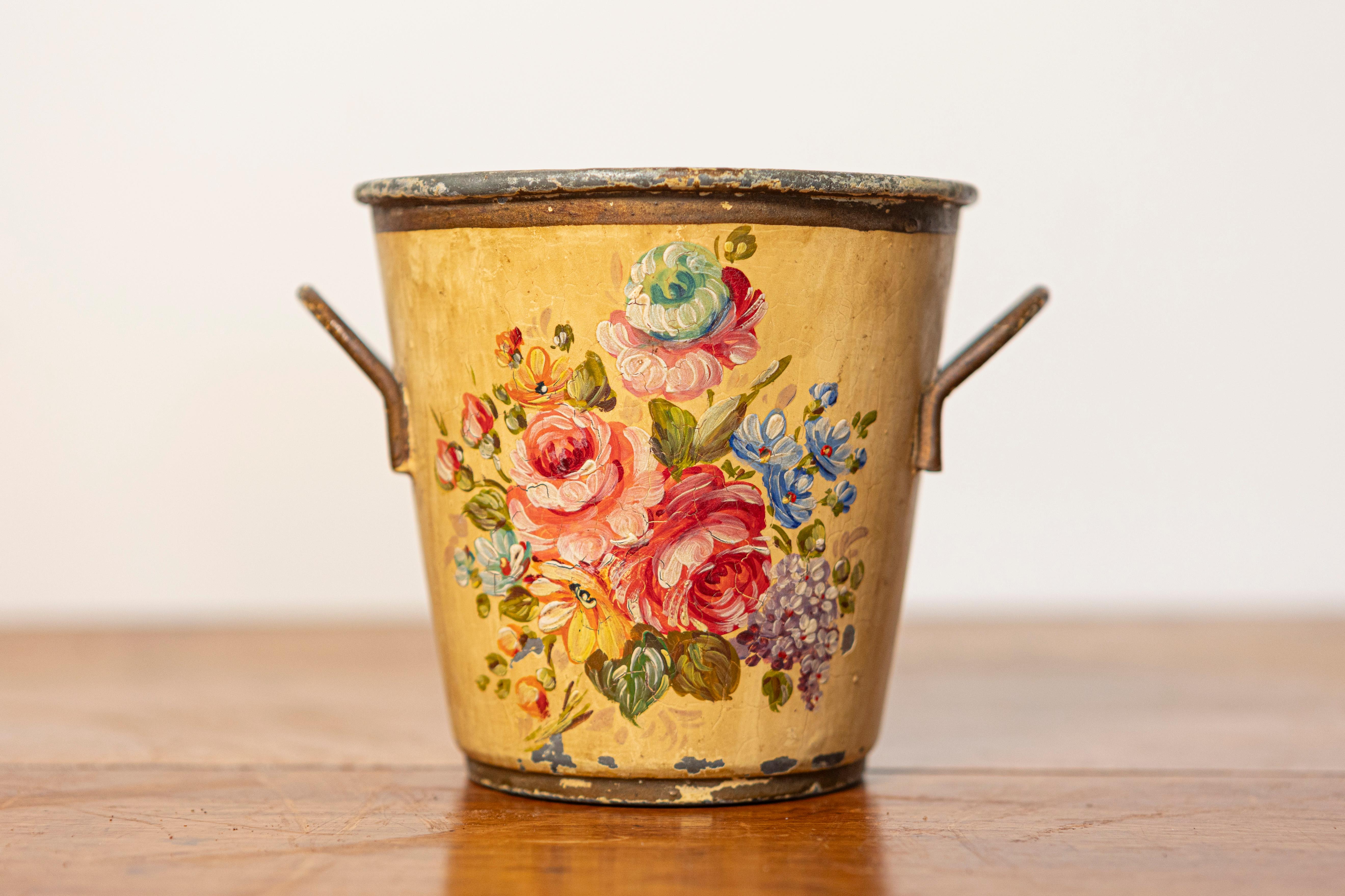 Questo piccolo cache-pot del XIX secolo è realizzato in lamiera verniciata e presenta una squisita decorazione floreale su uno sfondo giallo caldo. Gli intricati fiori dipinti a mano, tra cui rose rosa tenue e altre fioriture colorate, creano