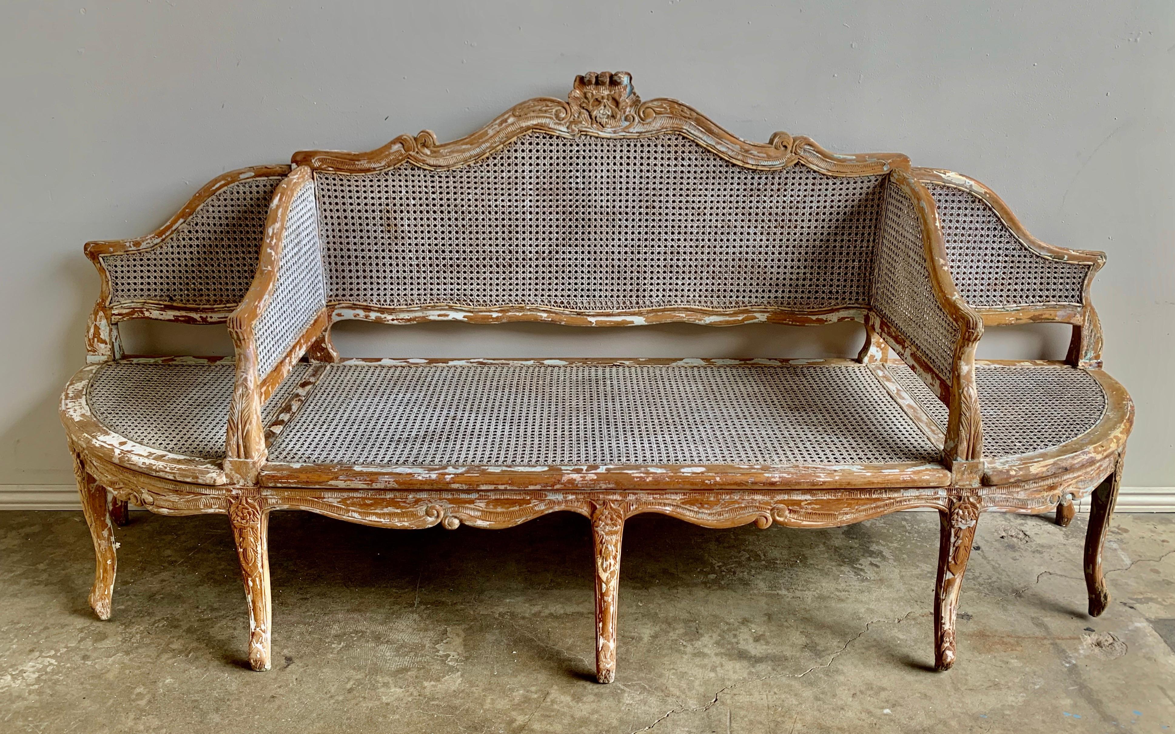 19th century part French carved cane settee. The settee stands on nine-cabriole legs with ram's head feet. There are remnants of paint that can be seen throughout the piece. Cushions can be made but it looks beautiful as it is.