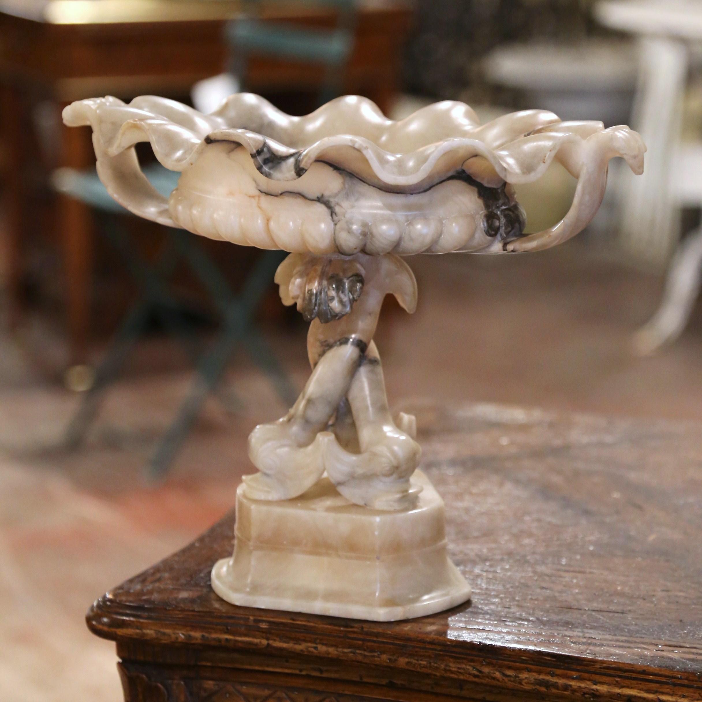 Decorate a dining table or a console with this elegant antique centrepiece. Created in France circa 1880 and made of alabaster, the compote stands on an integral triangular base. It features a oval dish with scalloped edges and dressed with side