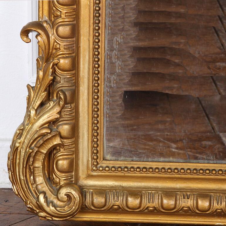 19th century French Louis XV style gilt mirror with a shaped and molded frame accented with scrolled carving at the bottom and elaborately carved top flourish. Retaining its original glass plate in good condition - expected and desirable 'patina' to