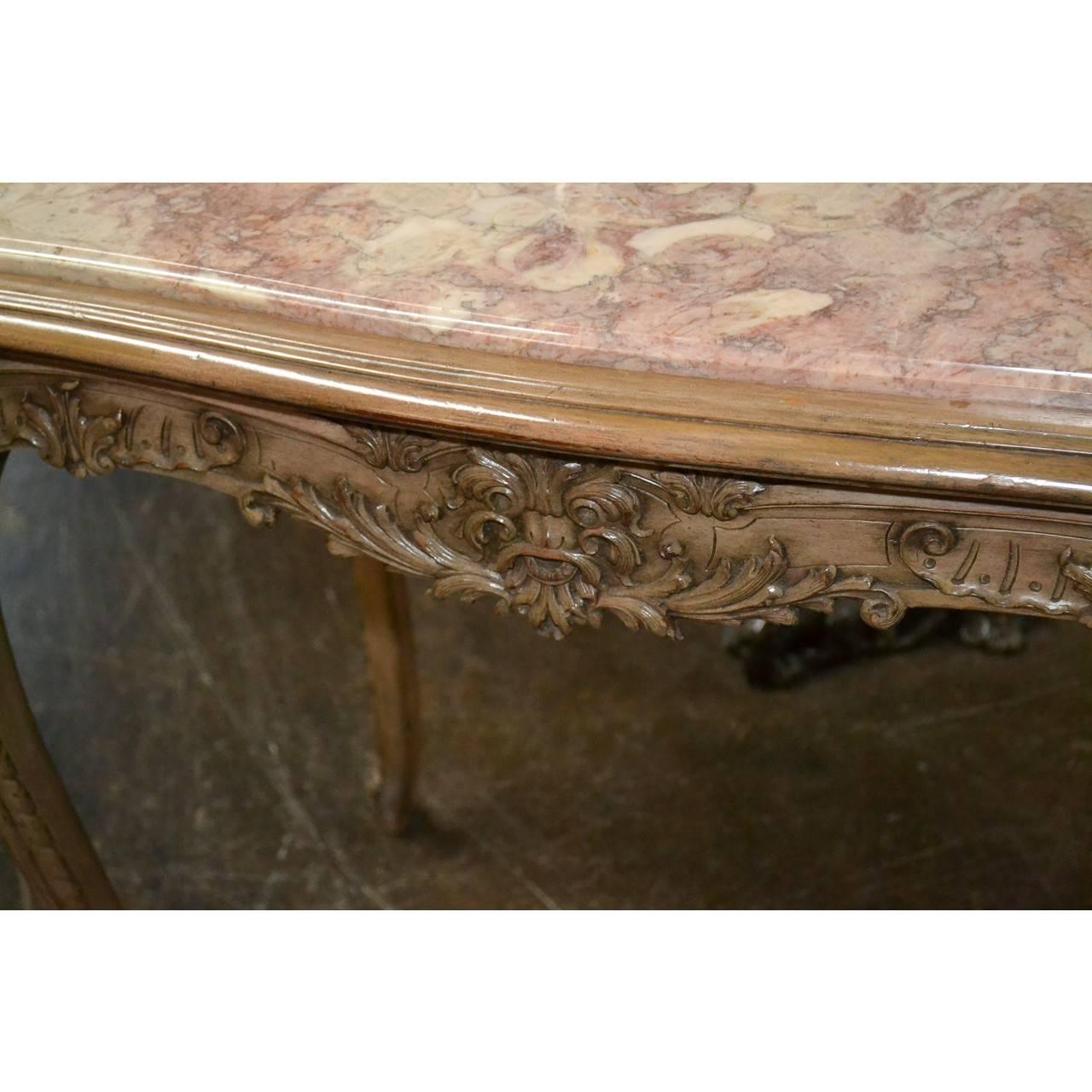 Very elegant and fine quality, 19th century French salon table with a serpentine shaped top inset with a gorgeous pale rouge, gray, and white marble. The carved wood and lacquered base with ornate acanthus leaf and fluer-de-lis accents on graceful