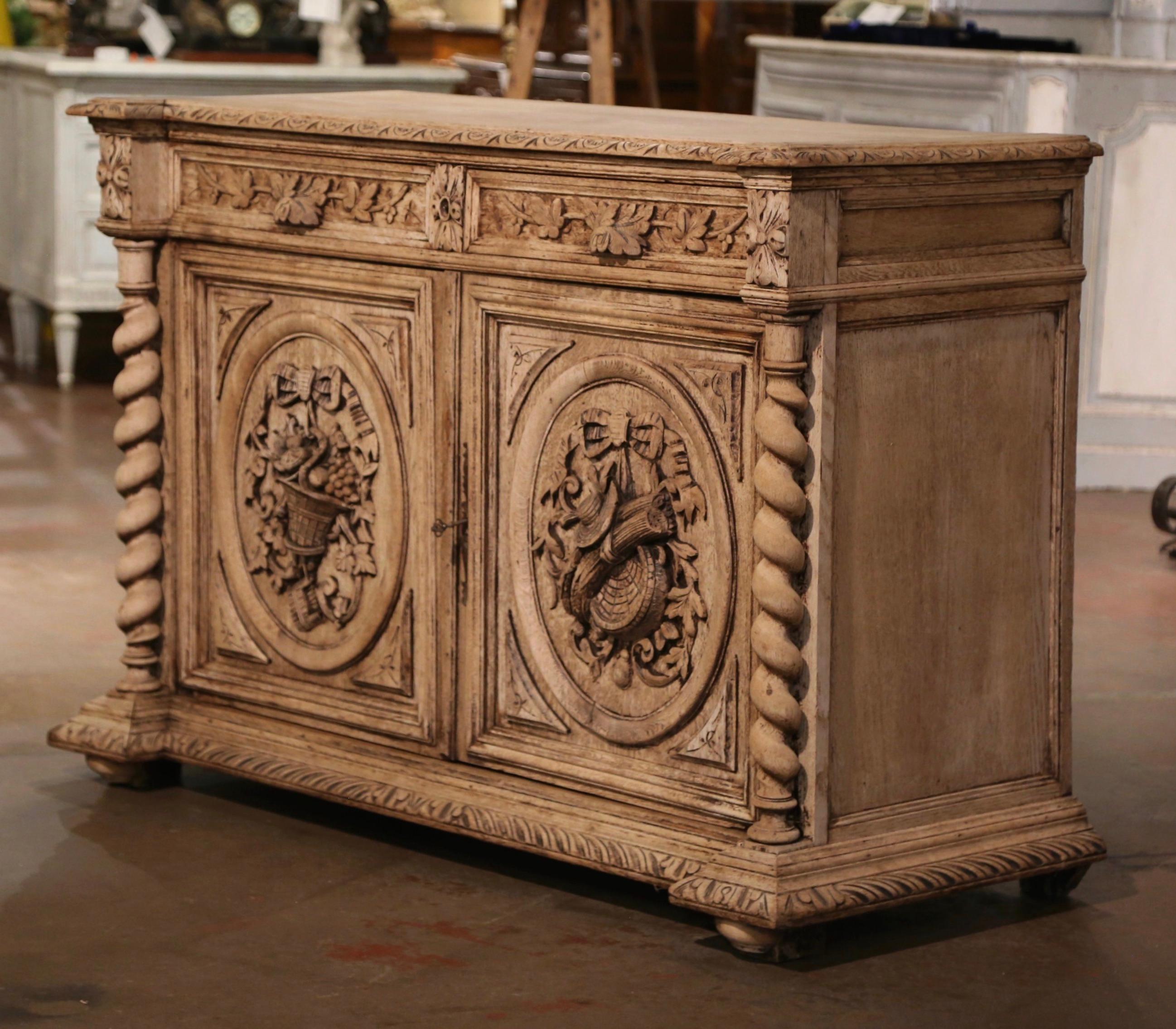 Decorate a den, a game room or an entry with this richly carved antique buffet! Created in France, circa 1860, and built of oak, the cabinet sits on front bun feet over a carved recessed base plinth, and embellished with barley twist side columns