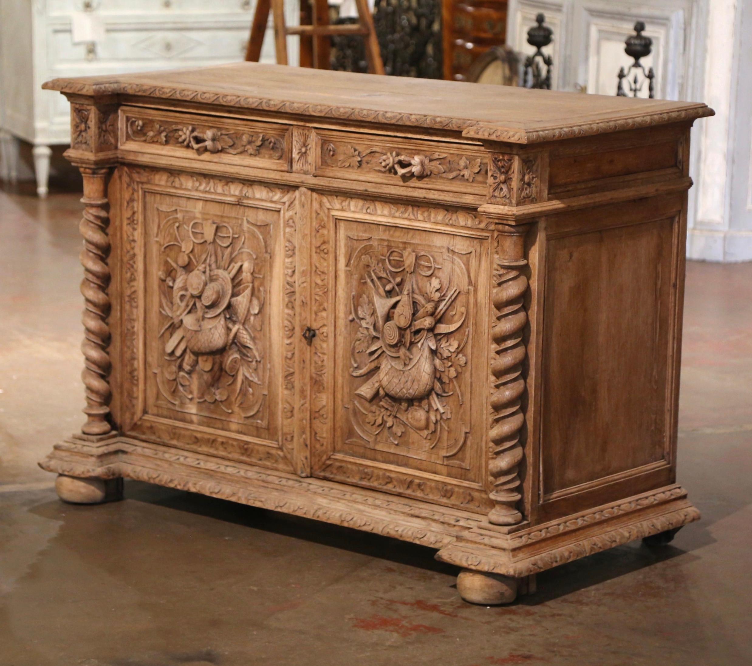 Decorate a den, a game room or an entry with this richly carved antique buffet! Created in France, circa 1860, and built of oak, the cabinet sits on front bun feet over a carved recessed base plinth, and embellished with barley twist side columns
