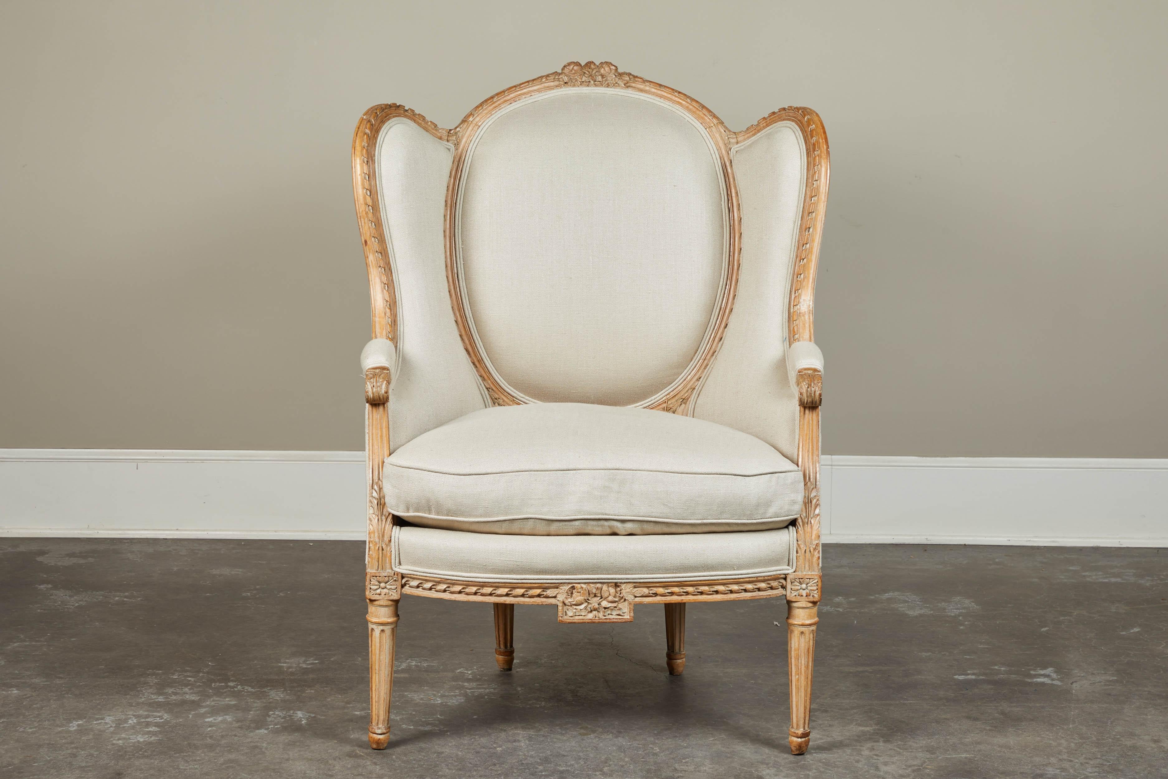 A very sweetly carved French wingback armchair with solid linen-look upholstery. Removable seat cushion and lighter wood trim, circa 19th century.