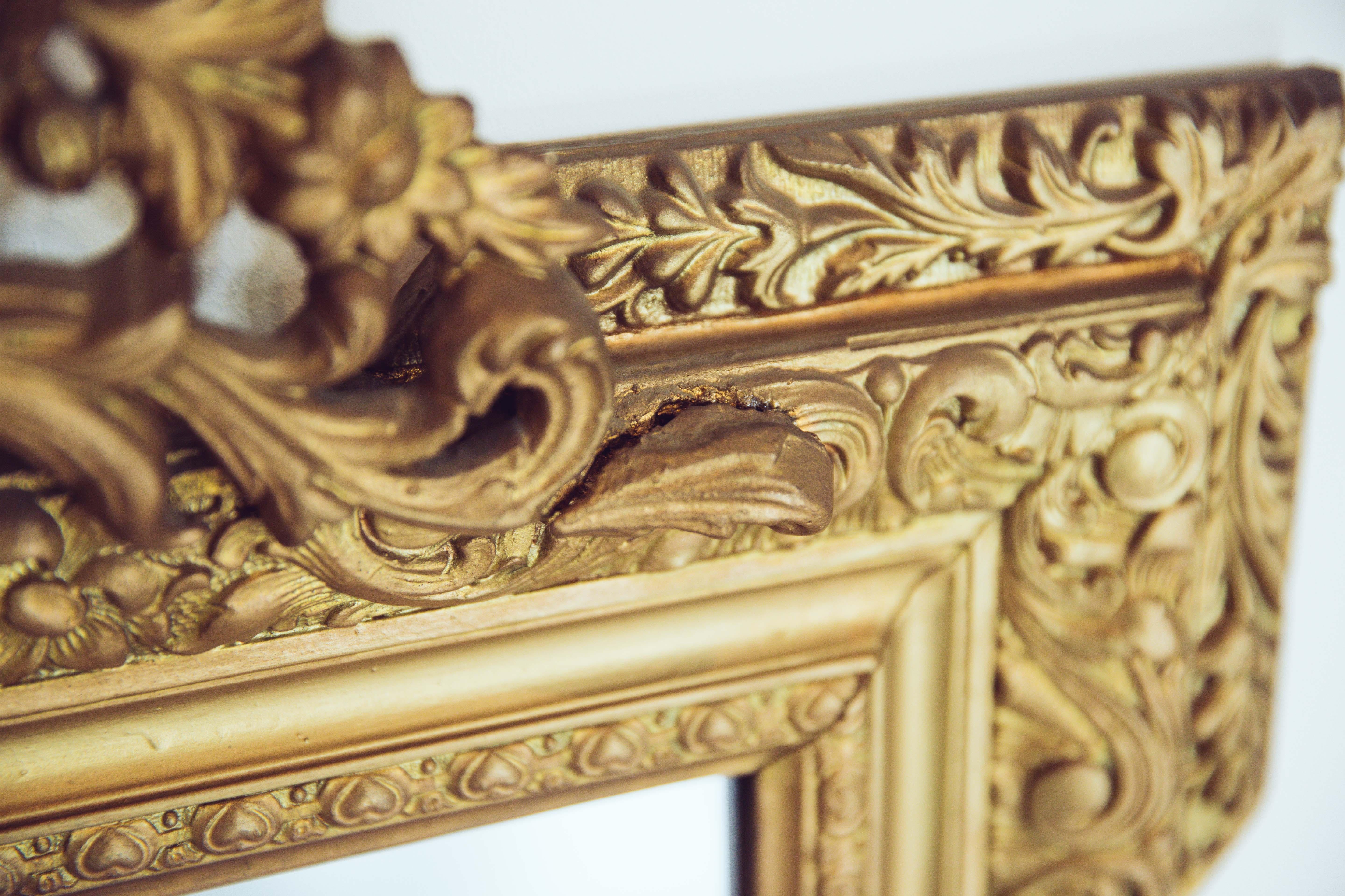 A French antique carved gilded wood mirror with urn crest. The frame displays carved flowers, leaves and little heart details. With four accented ornate corners.