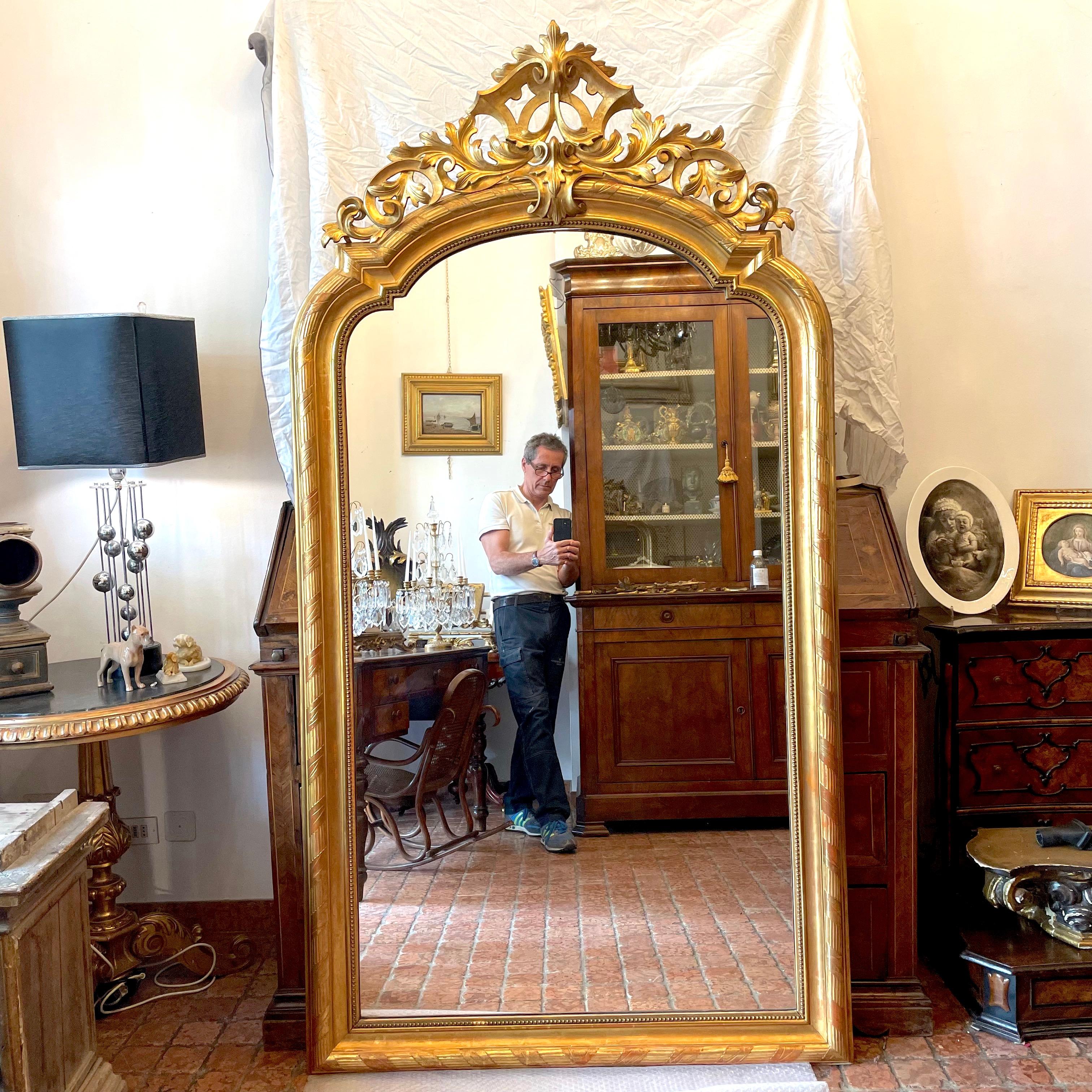 A stunning 19th century large French mirror with hand-carved and gold-leaf gilded wood frame, featuring an arched and pierced coping with deep scrolling and vegetal carving. Good condition, it comes from an antique palazzo of Milan downtown. This