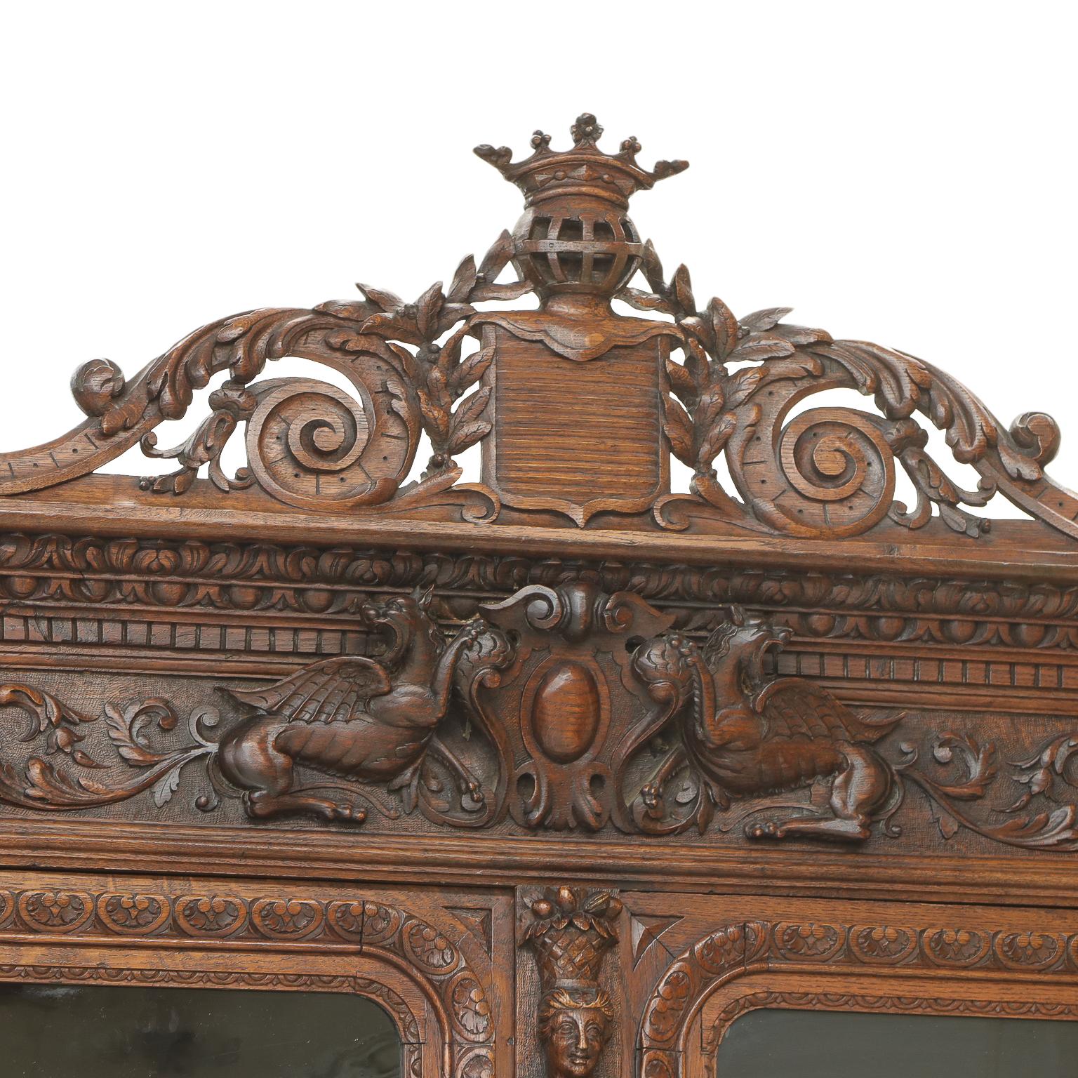 French oak hunting lodge cabinet topped with a distinctly rich, detailed Crown carved cornice. Lion and Sphinx carvings adorn the top of the cabinet with figural carvings down the side and middle framing two glass doors opening to a case with three