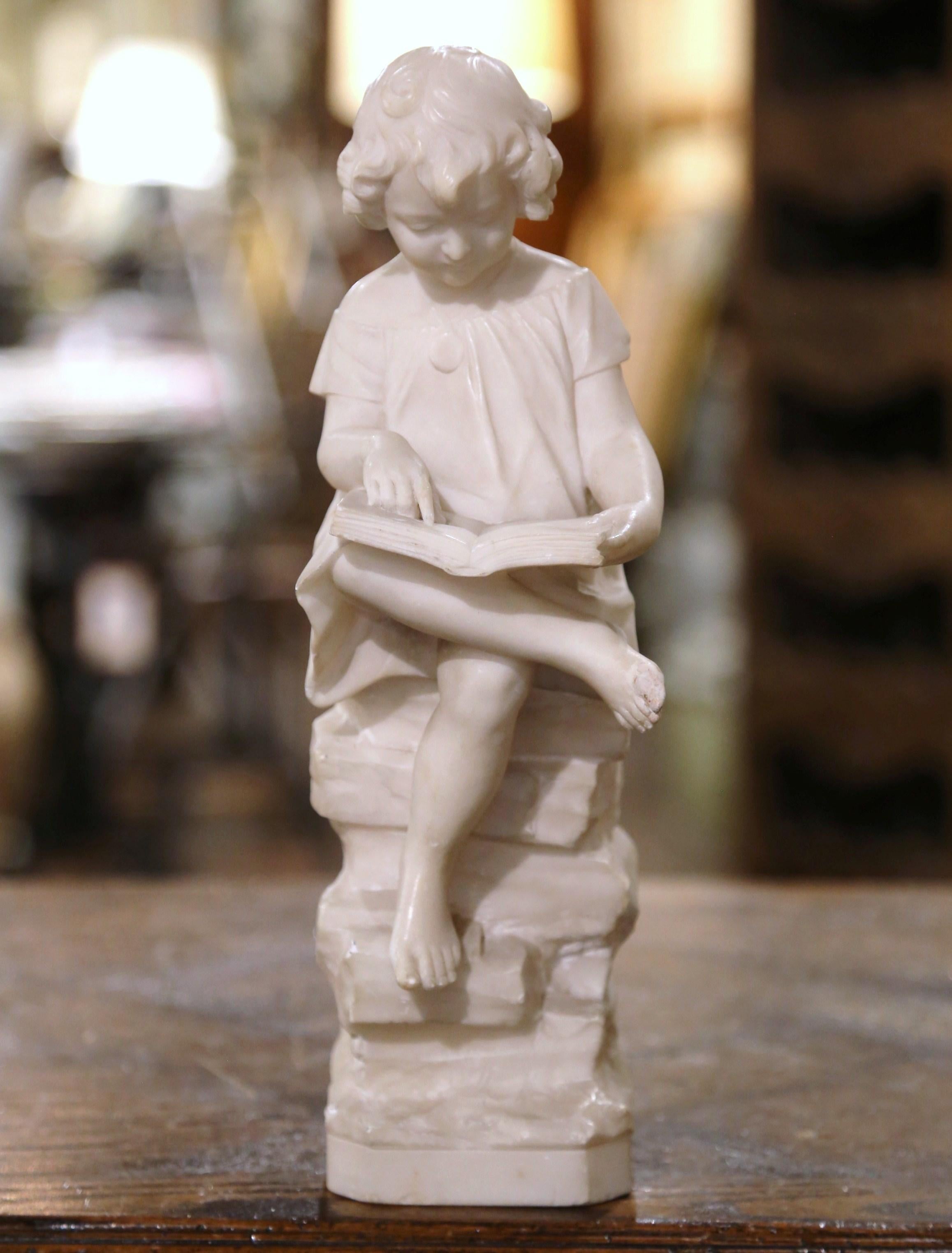 Decorate a shelf or a lady's desk with this adorable antique statue. Hand carved in France circa 1880, the marble statue stands on an attached square rocky form base, and depicts a young girl seated on a rock stool, and reading a book. One hand