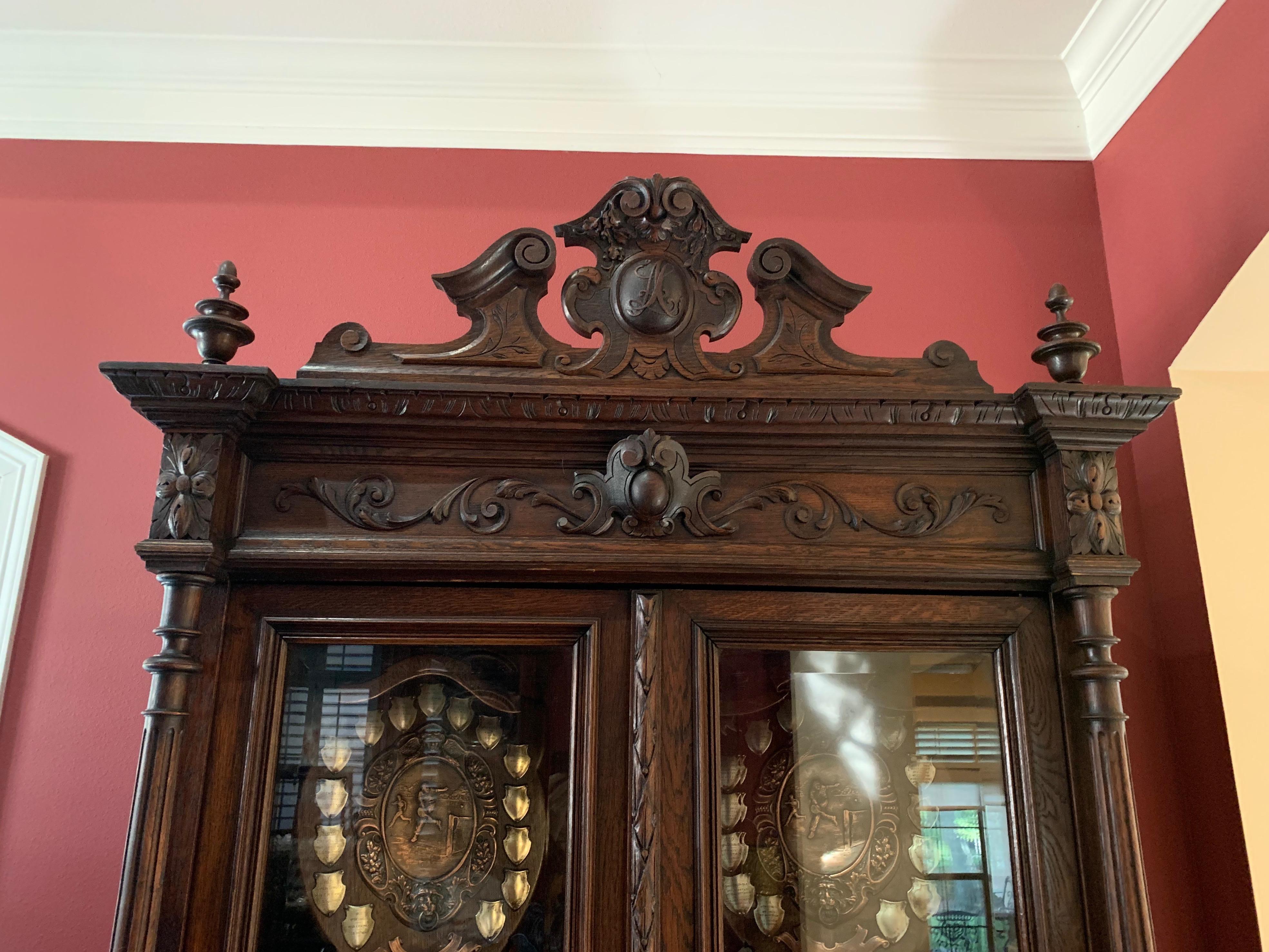 Direct from France, a majestic 8 ft. tall antique French bookcase with glass upper doors and distinctive renaissance style!
~The “broken pediment” style high upper crown features a center medallion hand carved with initials and flanked by two large