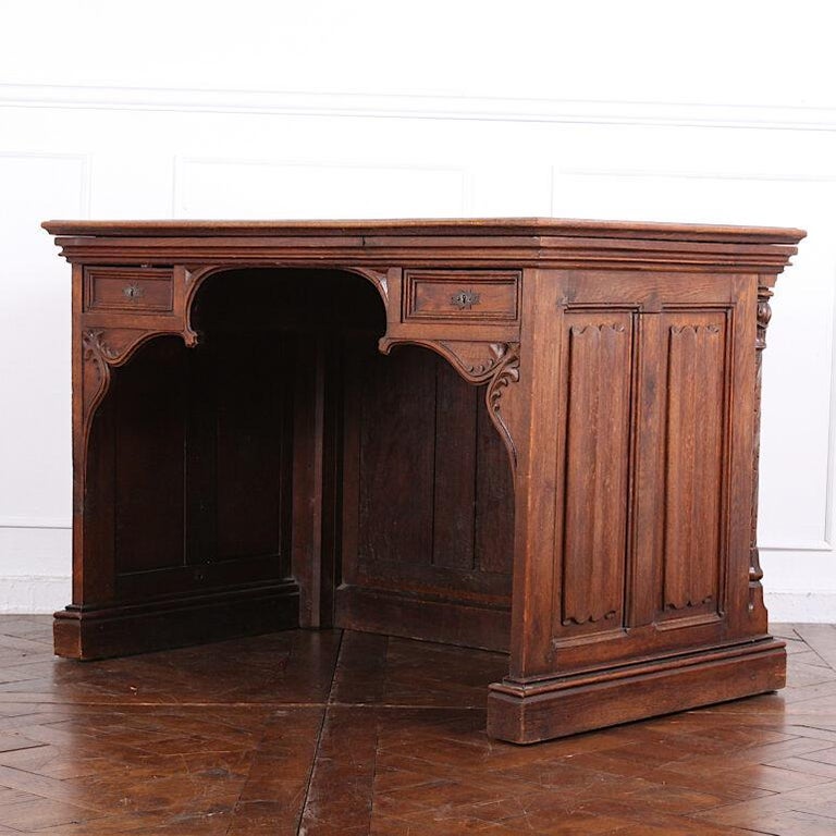 Highly carved French gothic desk in oak with ornately-carved panels to the front and linen-fold carving to each side and with turned and carved columns at the corners. Two small drawers fitted to either upper side of the knee hole. Likely an early