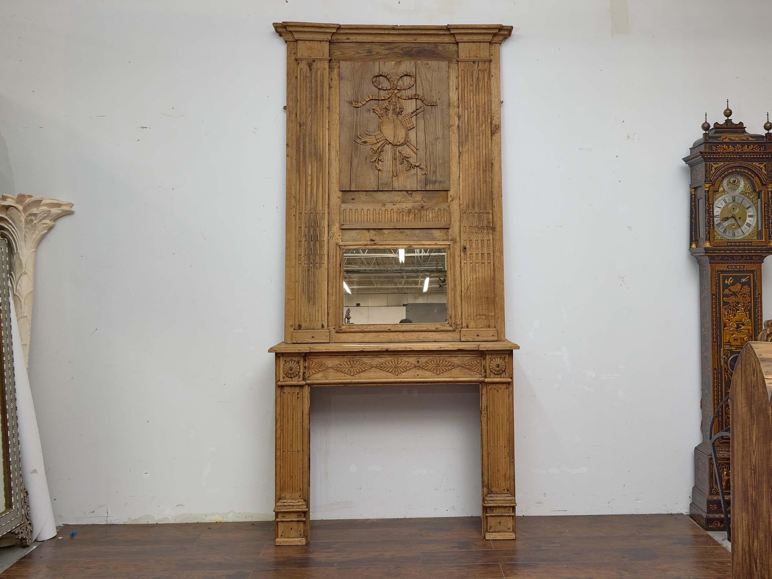 Important trumeau en chêne sculpté de style Louis XVI du XIXe siècle, composé de deux éléments distincts : un grand miroir à trumeau avec des motifs classiques sculptés et une base de cheminée coordonnée. L'échelle est impressionnante et