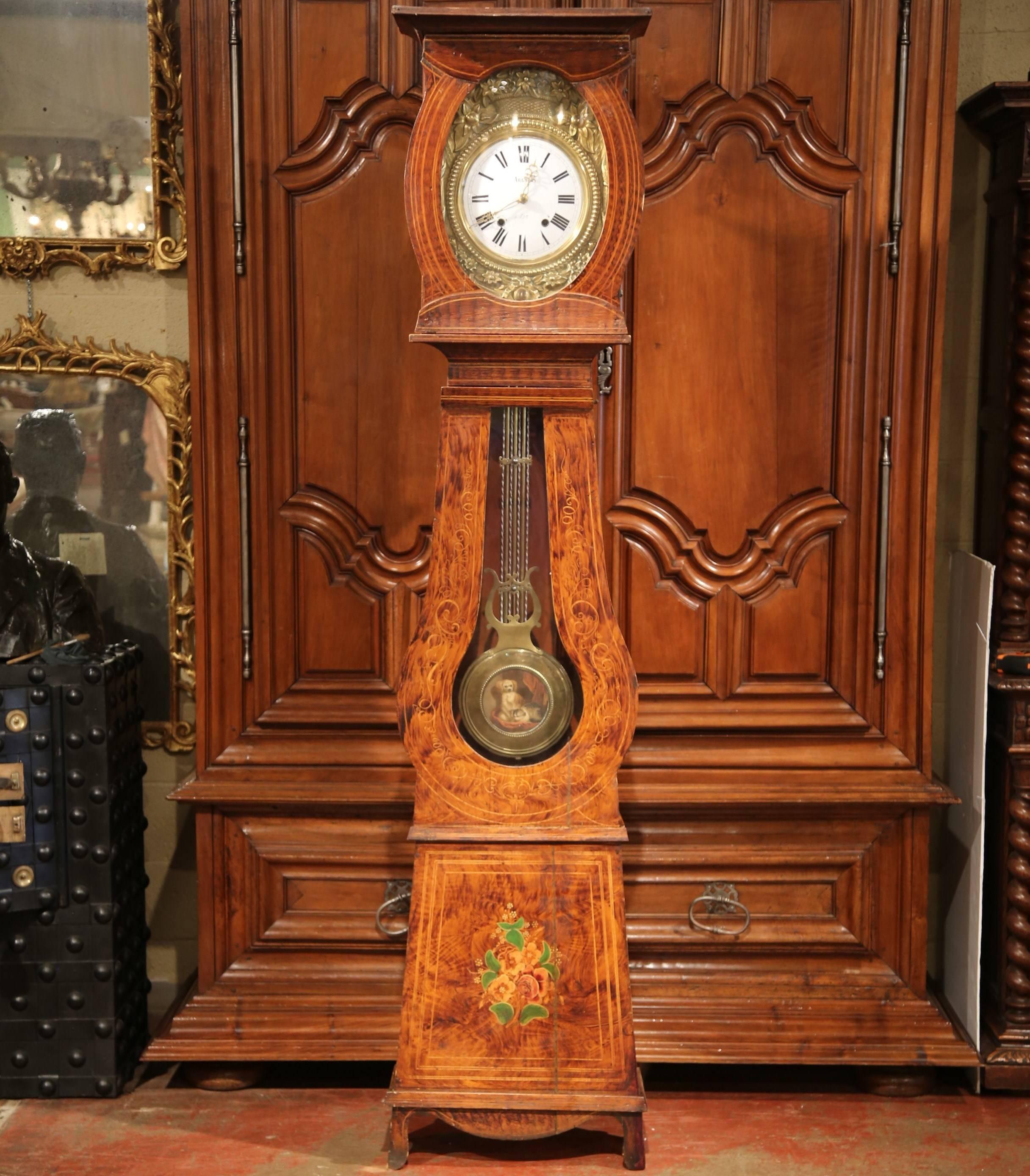 This elegant, painted long case clock was crafted in northern France, circa 1850. The tall, antique comtoise clock is nicely carved and features hand painted floral decor on the case. The brass clock face has a repousse floral and fruit decor, and