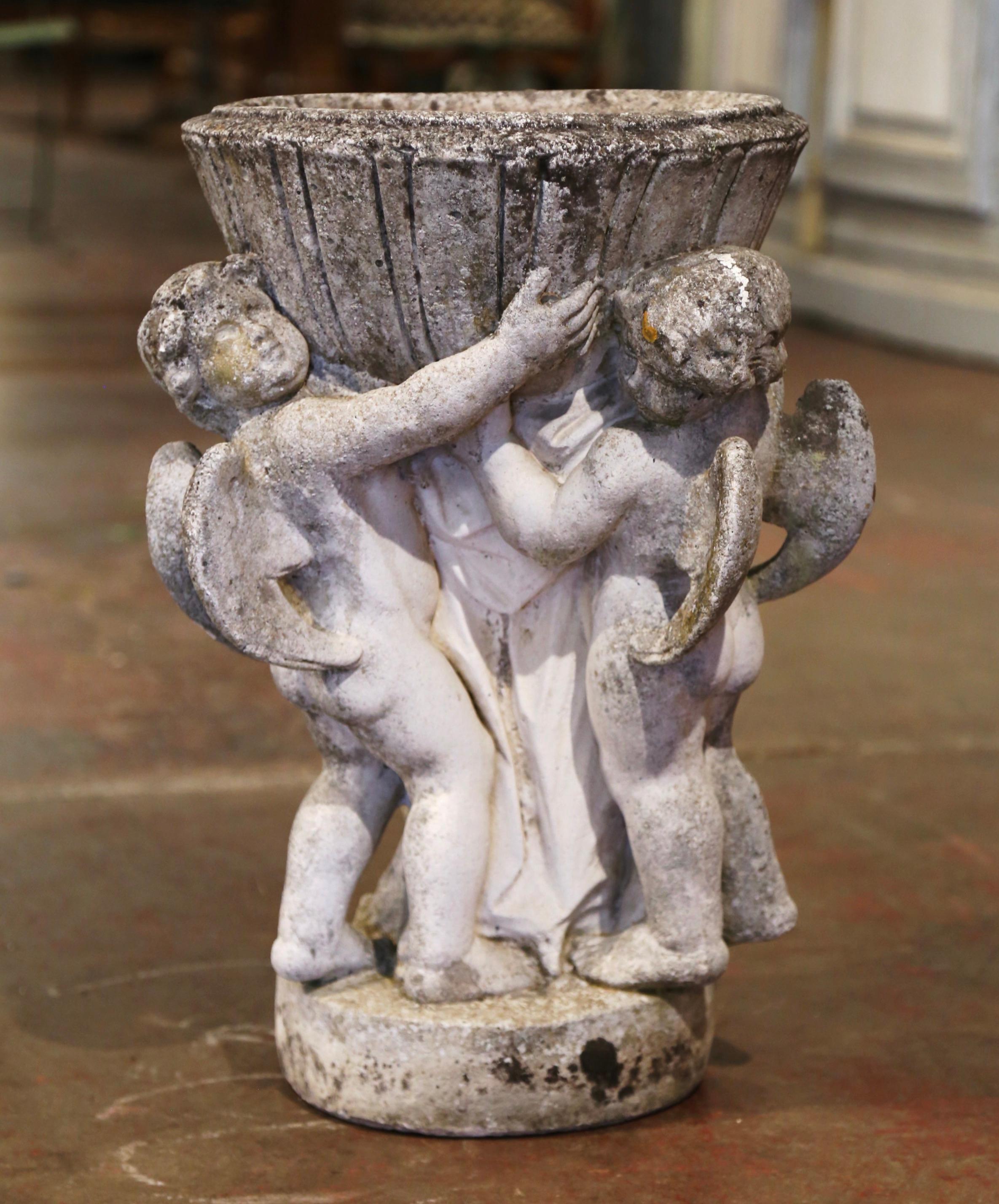 Decorate a garden or a patio with this antique outdoor planter. Crafted in Normandy France, circa 1860, and built in one piece, the stone flower pot stands on a round base, and features three carved winged putti holding the planter. The heavy
