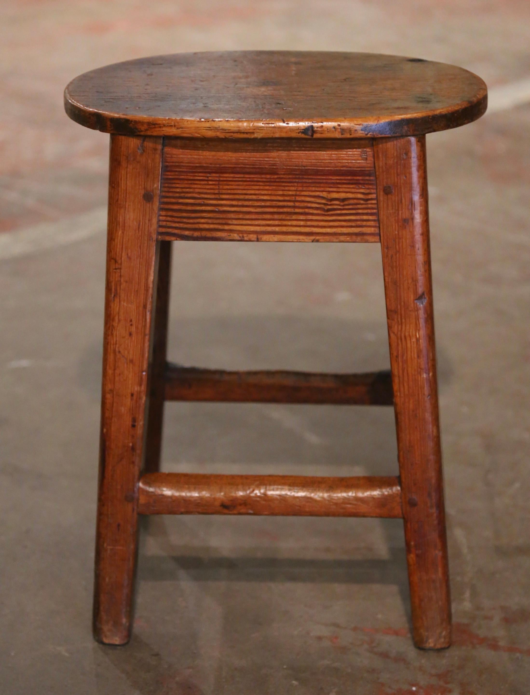 This antique country stool was created in Northern France, circa 1860, and was probably used to milk cows. Built of pine and oval in shape, the piece stands on four square legs connected with a sturdy stretcher at the bottom. The rustic stool is in