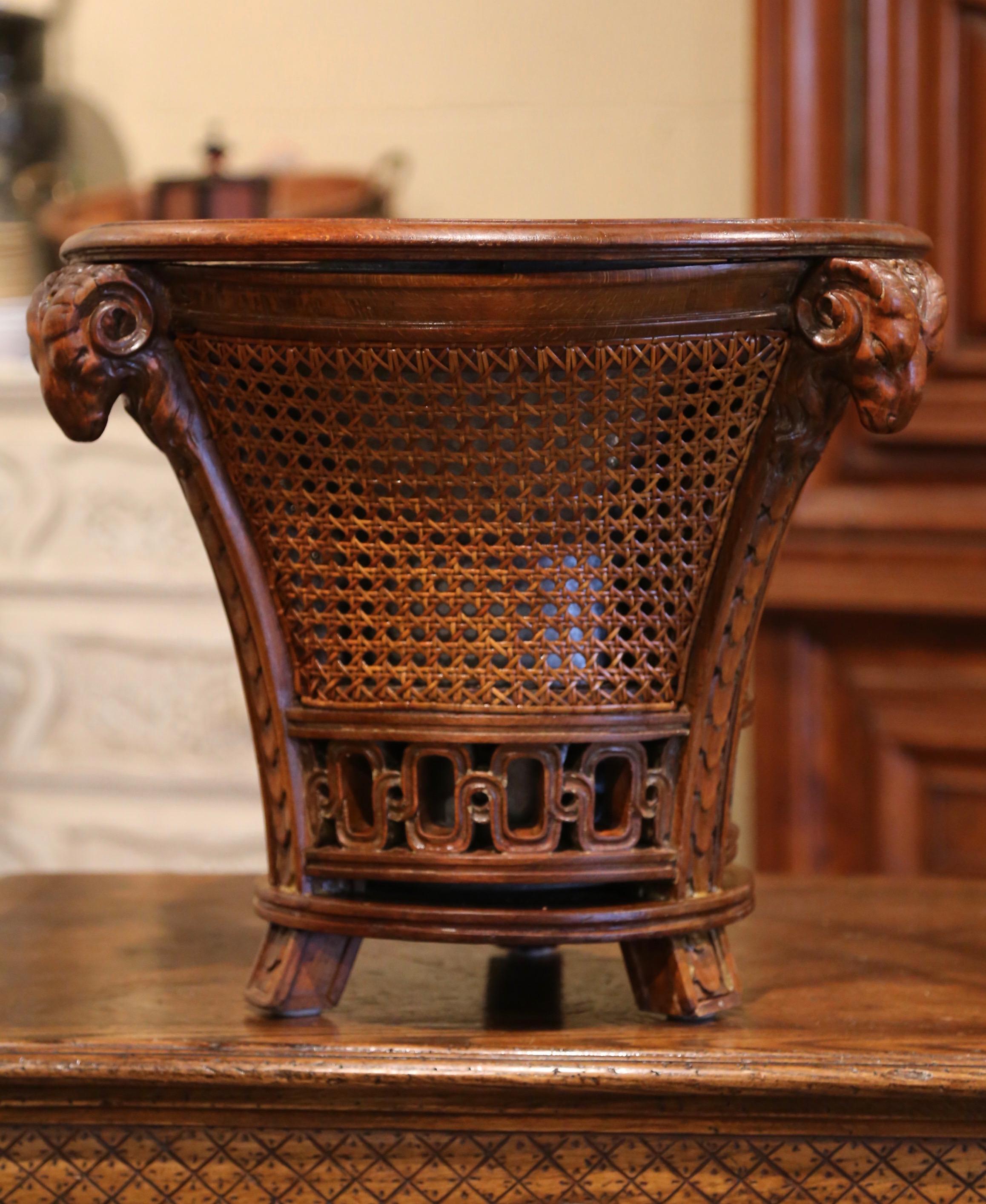 This elegant antique planter was crafted in France circa 1860; made of walnut and hand woven caning, the jardiniere is decorated with three ram head sculptures at the pediment further embellished with a carved pierced rim at the base over the small
