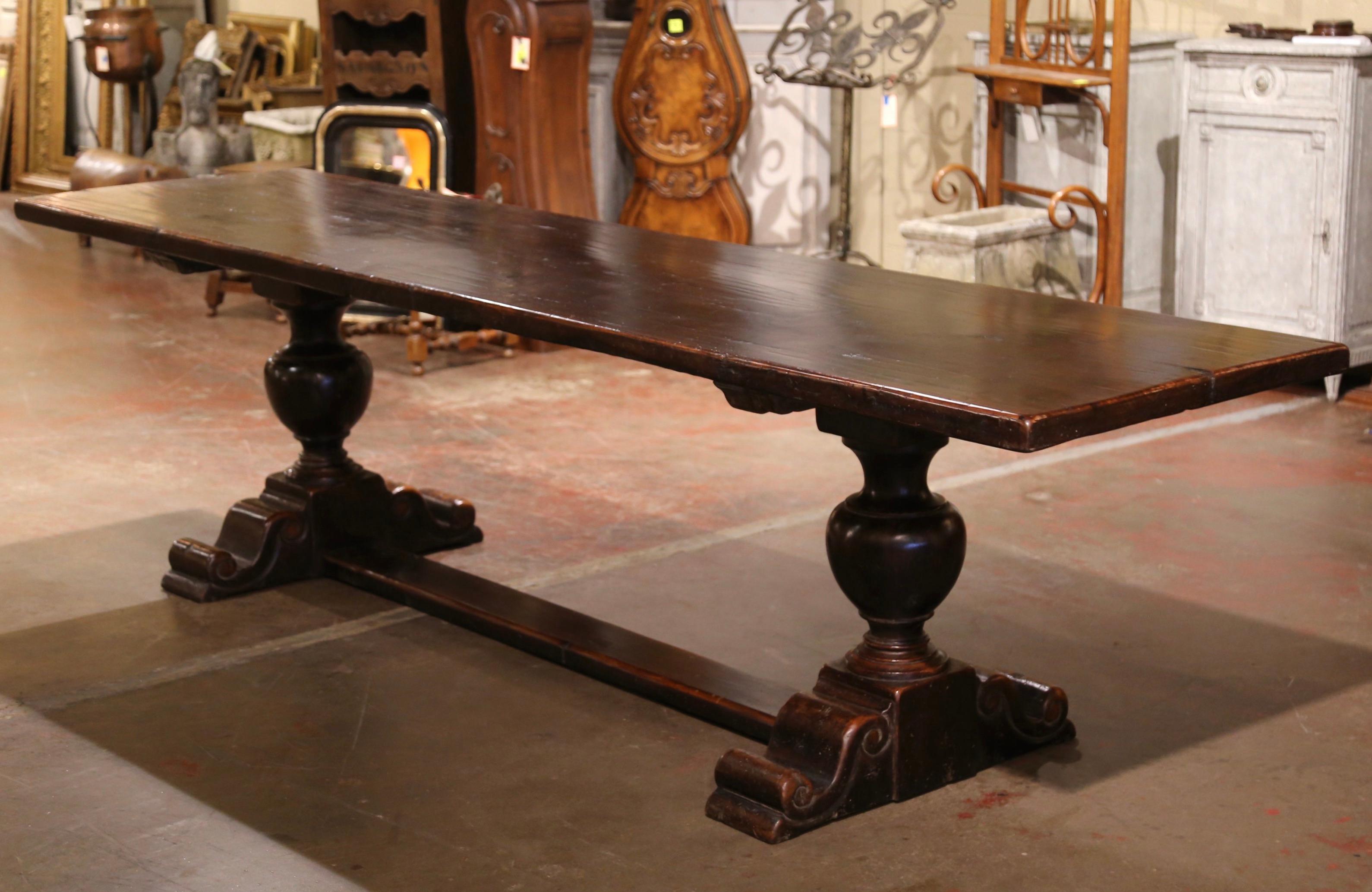 This elegant antique 10 foot monastery dining table was crafted in France, circa 1850. Standing on two carved turned pedestal legs ending with shoe base and joined by bottom stretcher attached with key and tenon, the provincial table is dressed with