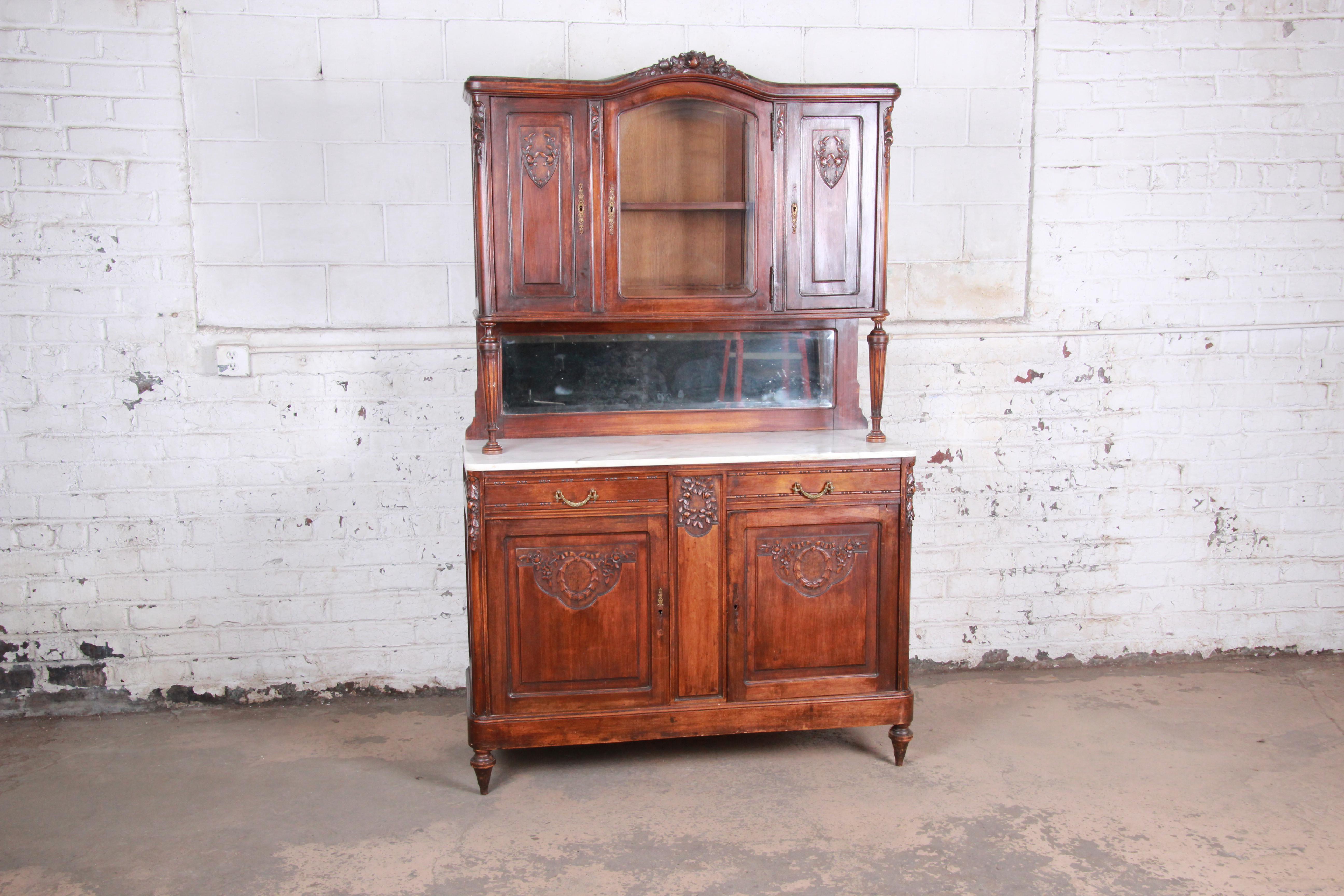A gorgeous 19th century French carved walnut marble top sideboard or bar cabinet. The cabinet features solid walnut construction with stunning carved wood details. It has a beautiful white marble top with mirrored backsplash. The cabinet offers