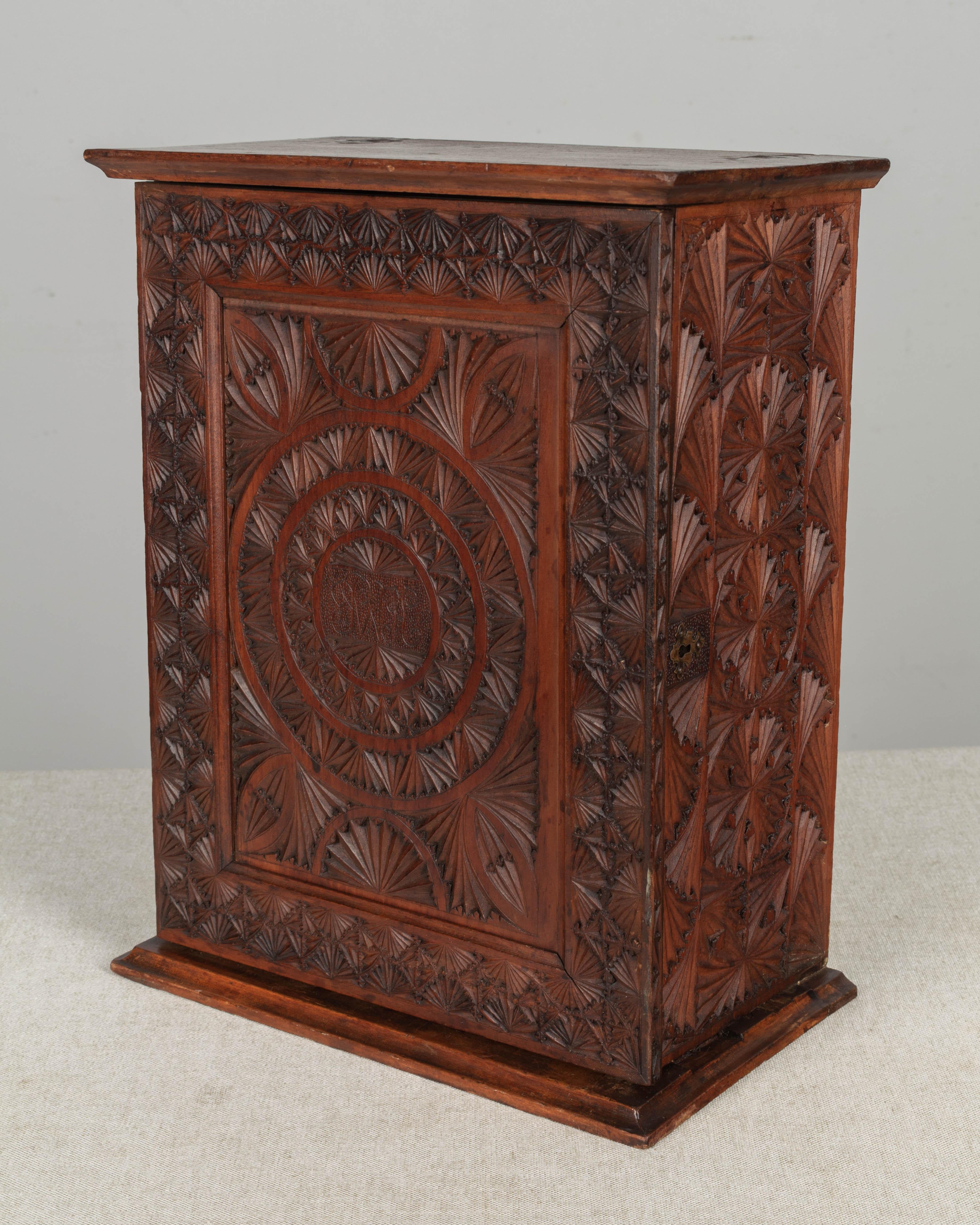 A 19th century French carved wooden box or small cabinet, perhaps for spices, with hinged door, opening to an interior shelf and two small drawers. Intricate geometric carving with monogram initials in the center of the door. No key.