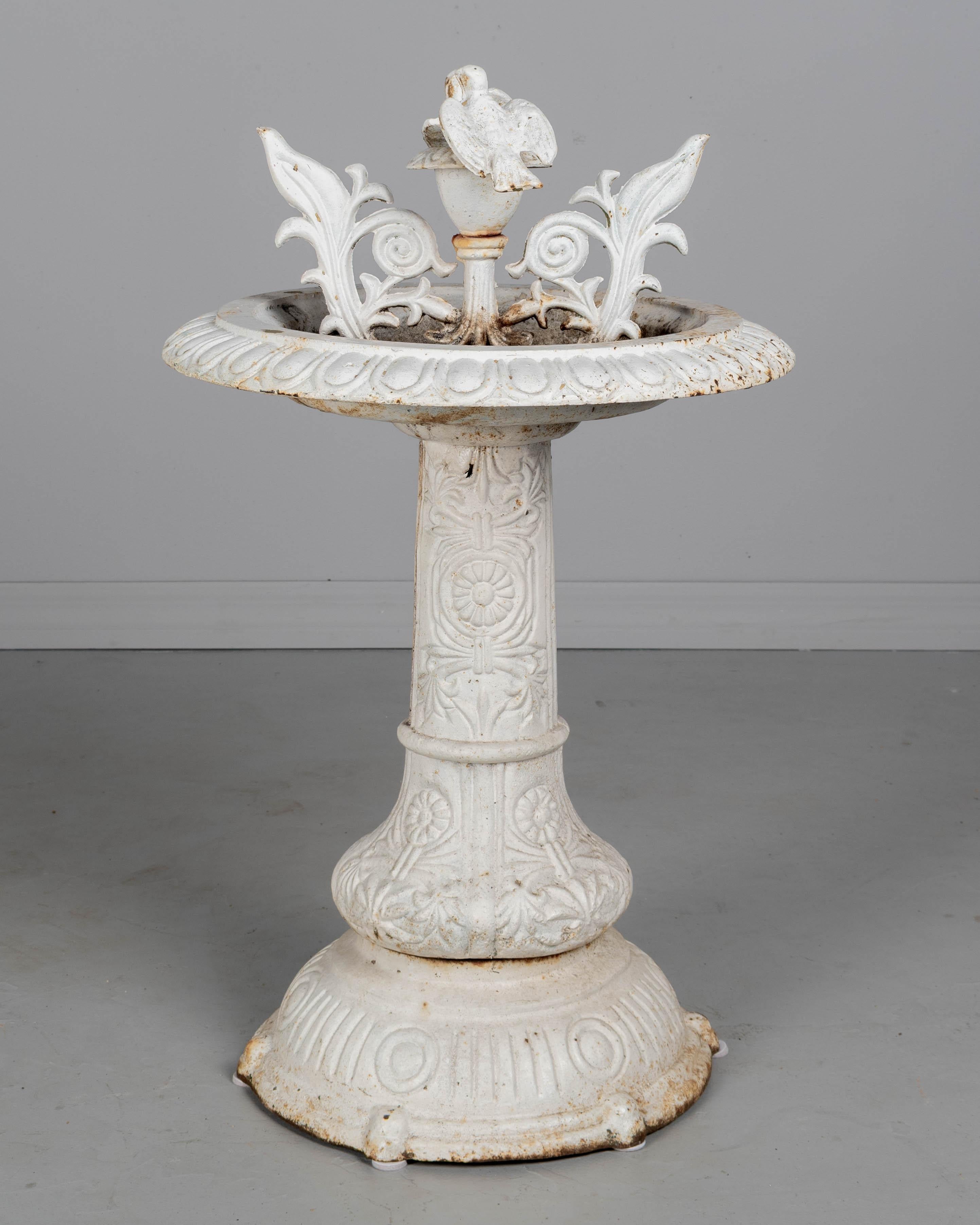 Una fontana in ghisa del XIX secolo con una coppia di uccelli appollaiati al centro di una vasca poco profonda. Pesante base a piedistallo con rilievi floreali stilizzati. La patina originale verniciata di bianco è in buone condizioni con patina