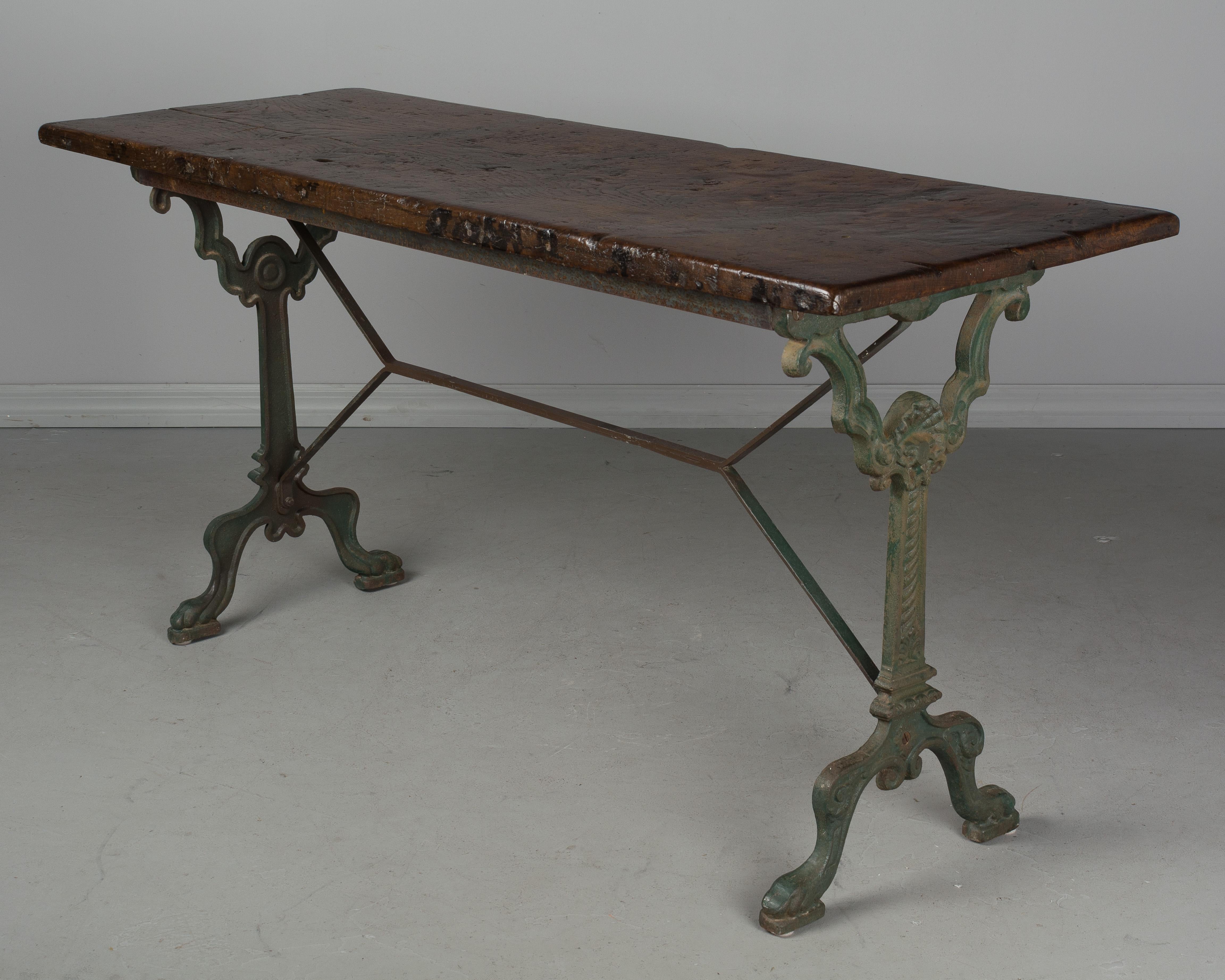 A 19th century French cast iron bistro table with rusty green painted patina and wood top. Top is as found with a beautiful one inch thick plank of old chestnut. Lovely character and patina of the wood with several knots and patterned grain. Waxed