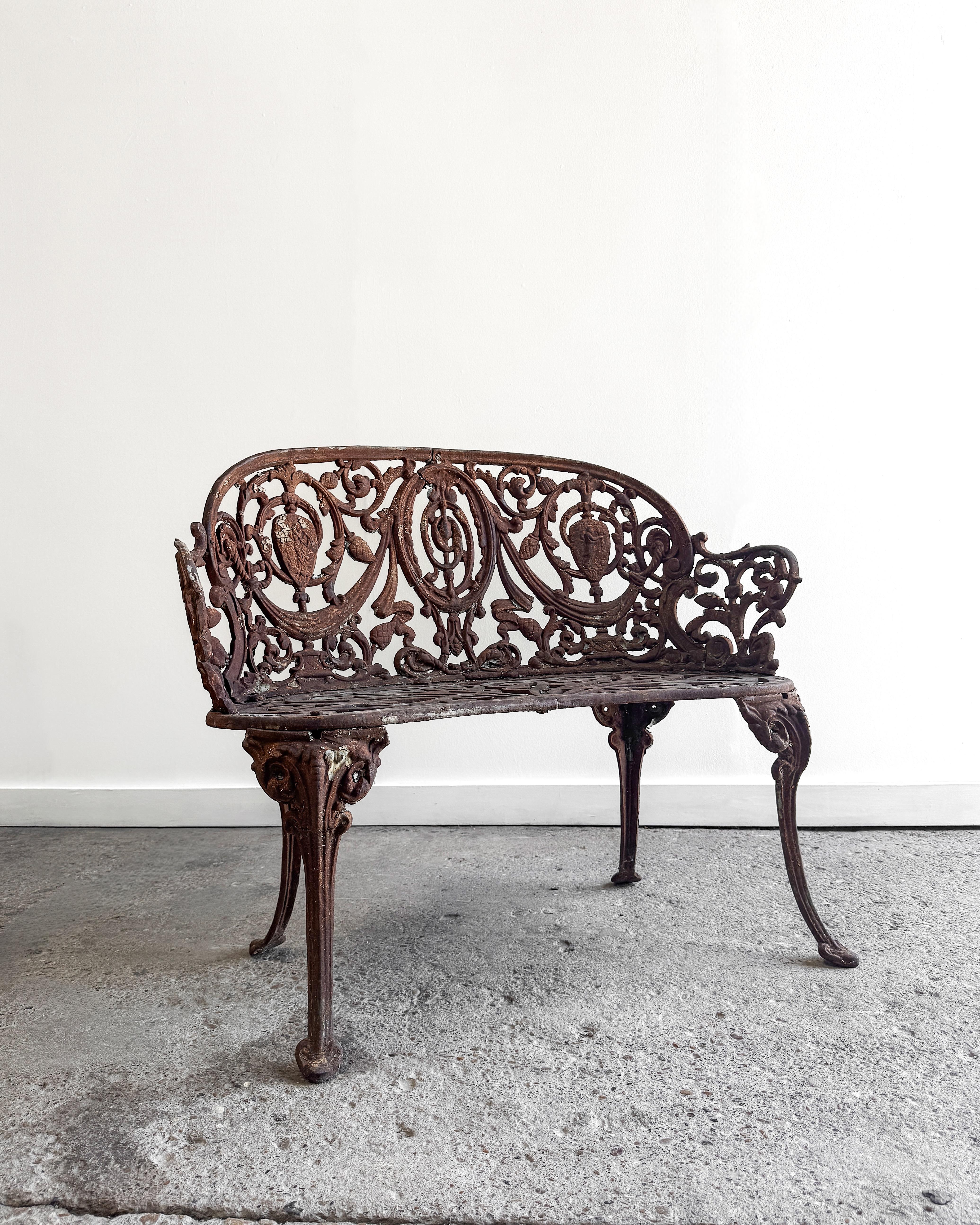 A beautifully detailed 19th-century French cast iron garden settee, showcasing the artistry of classical garden furnishings of the Victorian era. Featuring an intricate pierced back with scrolling foliage, grapevine motifs, and classical urn