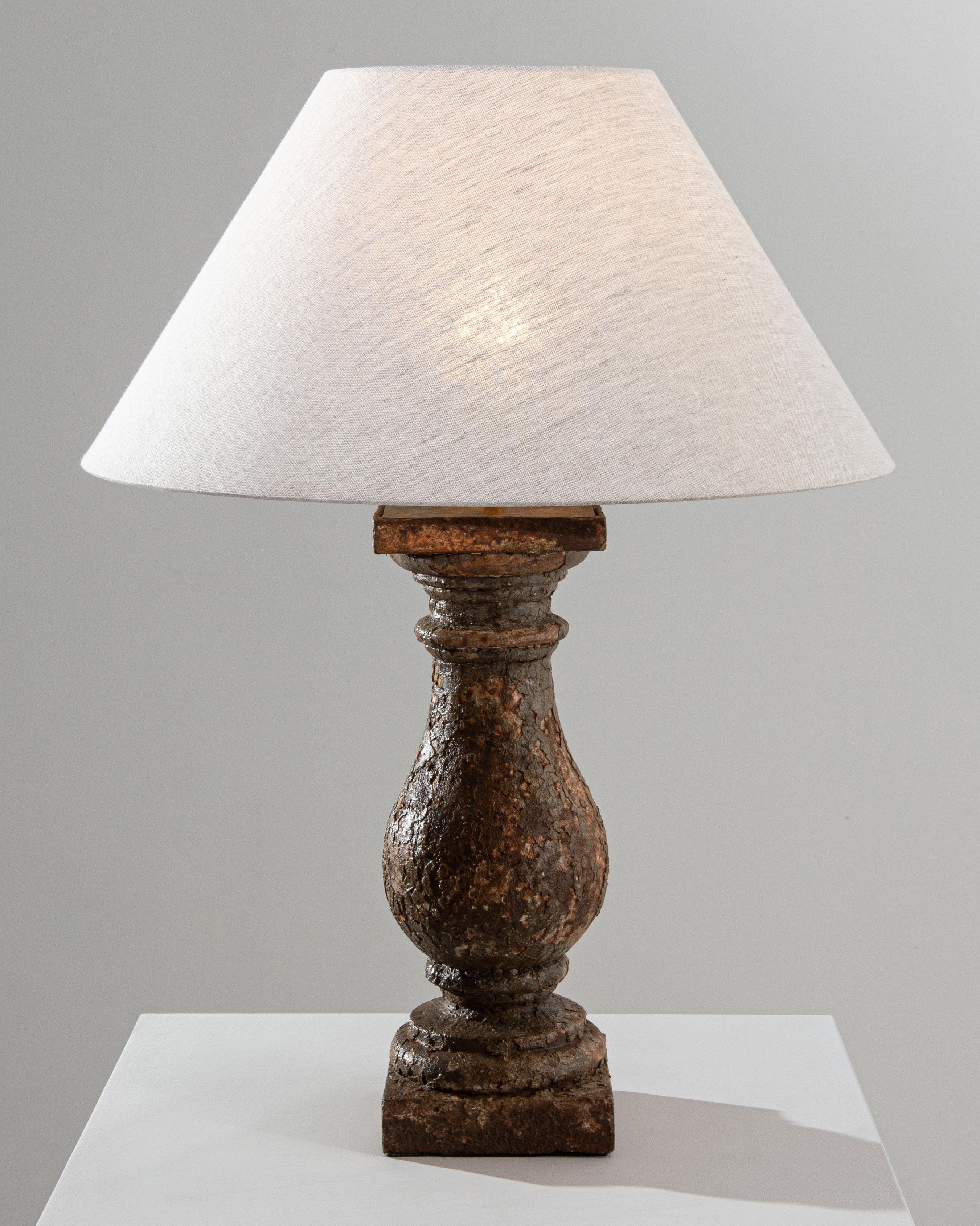 Confounding and timelessly elegant, this solid metal lamp, made from a 19th century French architectural element, impresses at first sight. With age, the surface of the cast iron base has slowly patinated, creating a compelling collage of browns and