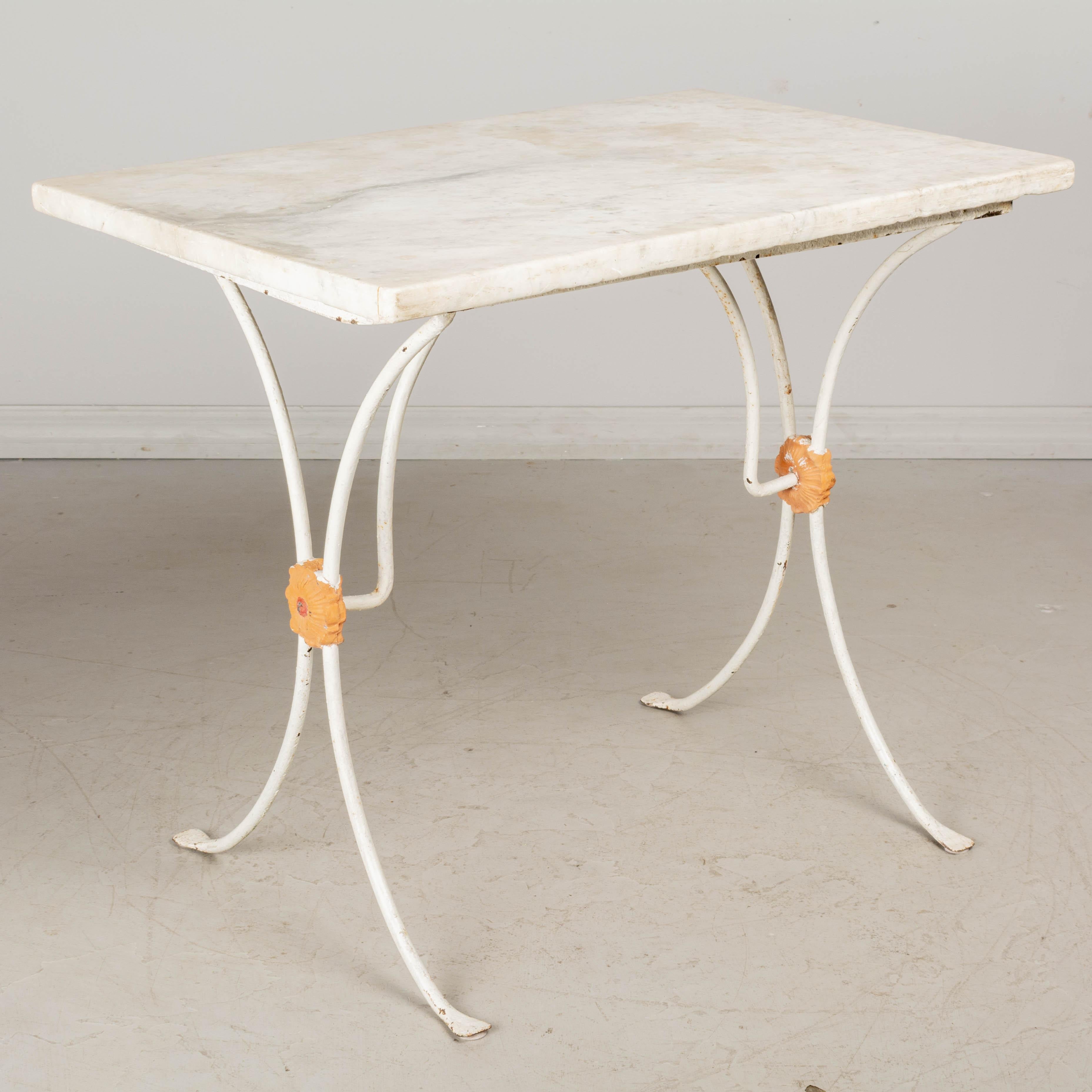 A 19th century French cast iron bistro table with white painted finish and original white veined marble top. Nice casting with orange painted rosette medallion detail. Minor paint loss. Marble has a hairline crack. Please note that the marble rest