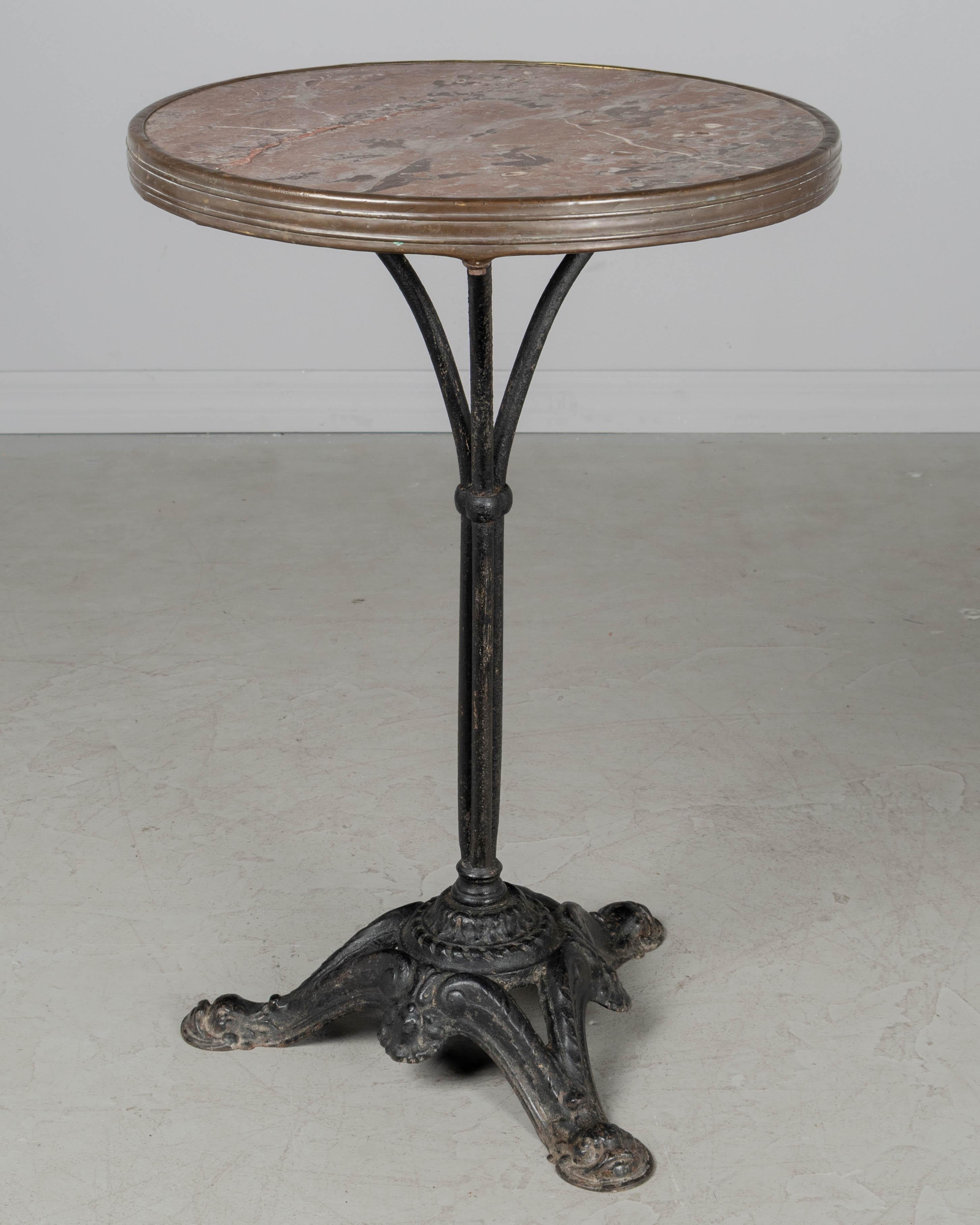Tavolo da bistrot francese in ghisa del XIX secolo con base a piedistallo. Colata pesante di buona qualità con piedi a testa di delfino e patina nera. Piano originale in marmo venato rosso e grigio con fascia in ottone lungo il perimetro.