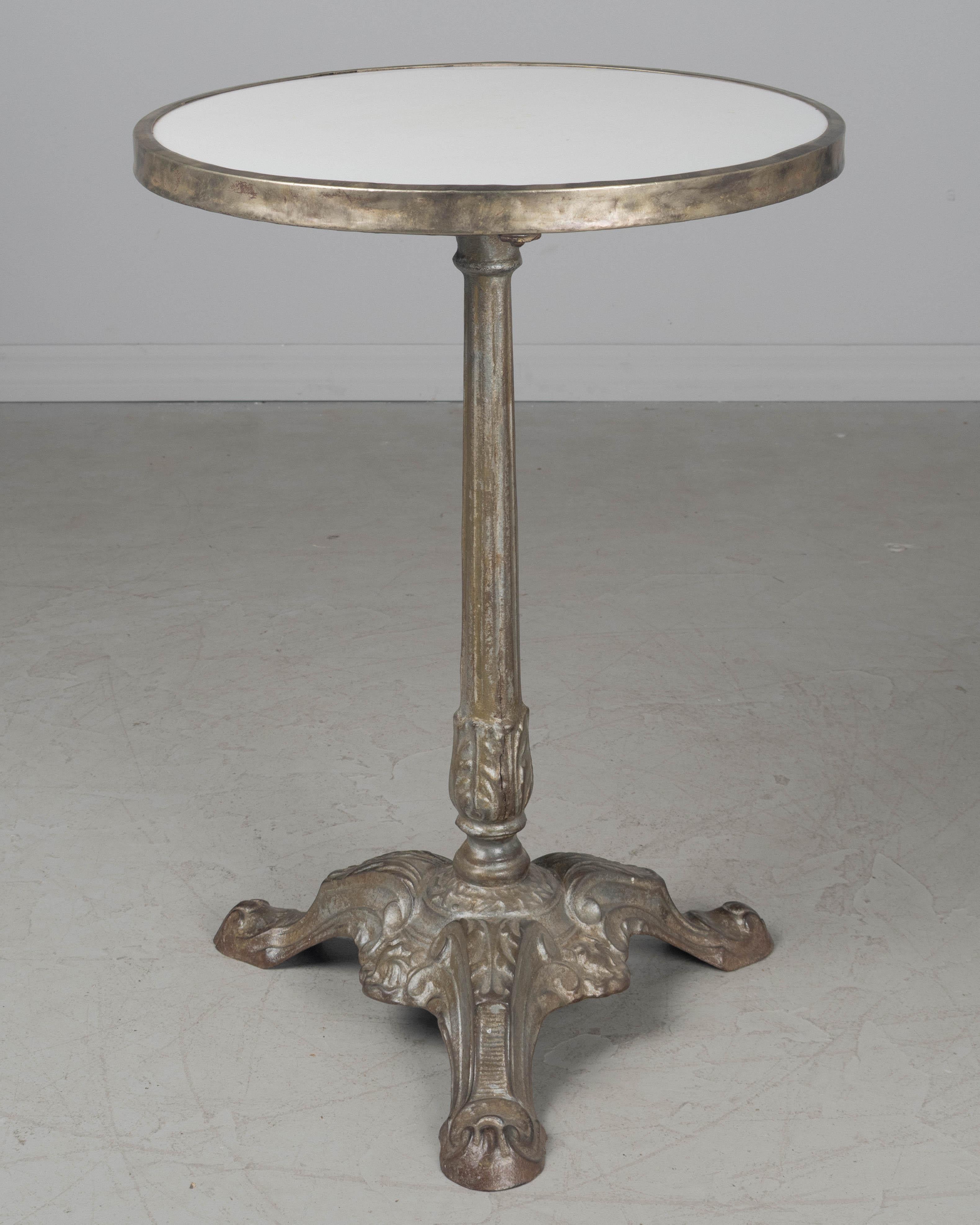 Tavolo da bistrot francese in ghisa del XIX secolo con base a piedistallo. Colata pesante di buona qualità. Ad un certo punto è stata tolta la finitura verniciata. Patina grigia calda con leggera ruggine. Piano in marmo bianco con fascia in ottone