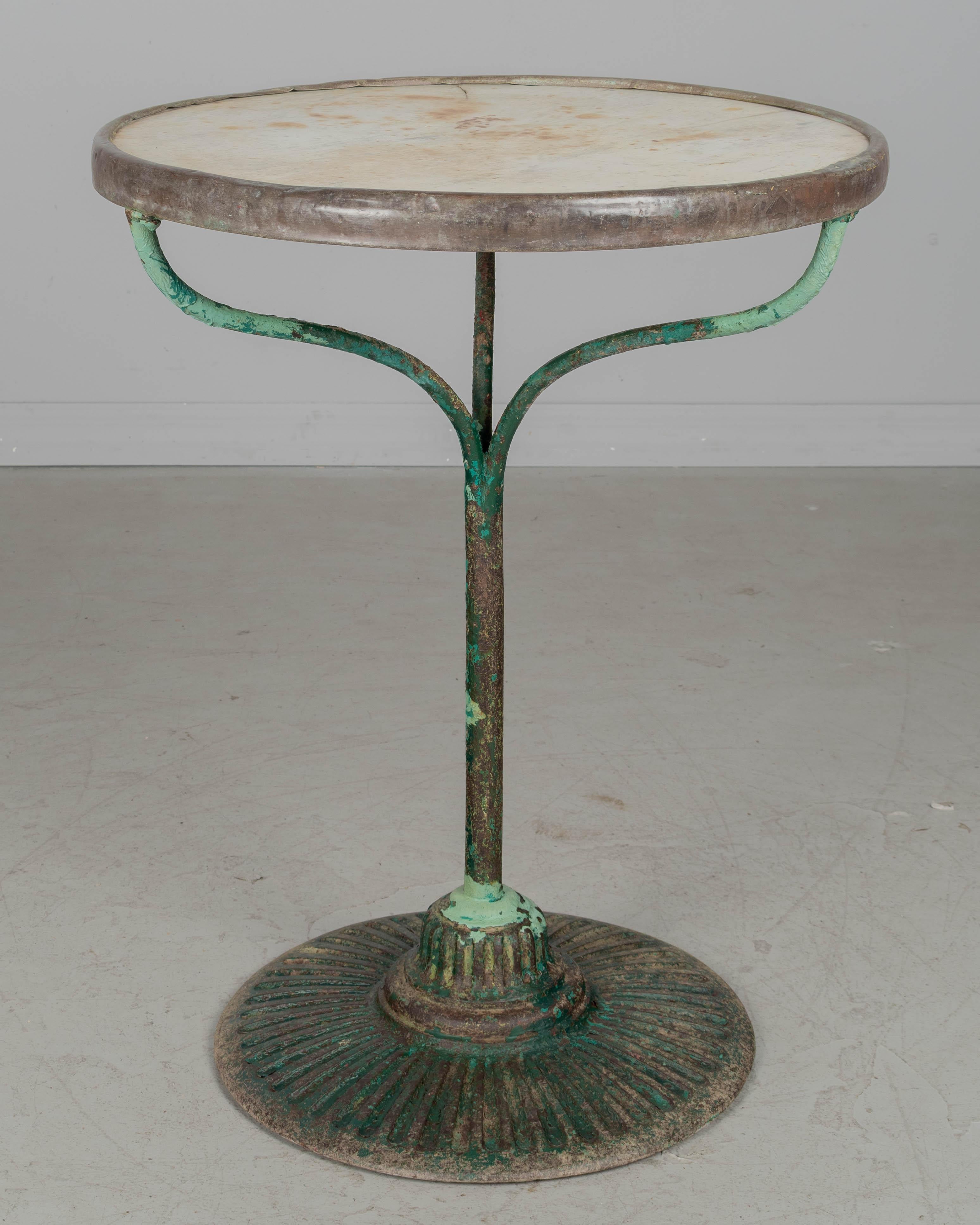 A 19th century French cast iron bistro table with pedestal base. Nice patina with layers of green paint. Original white marble top with brass band around the perimeter. Good quality heavy casting. Rust stains in marble. Table has a slight slant.