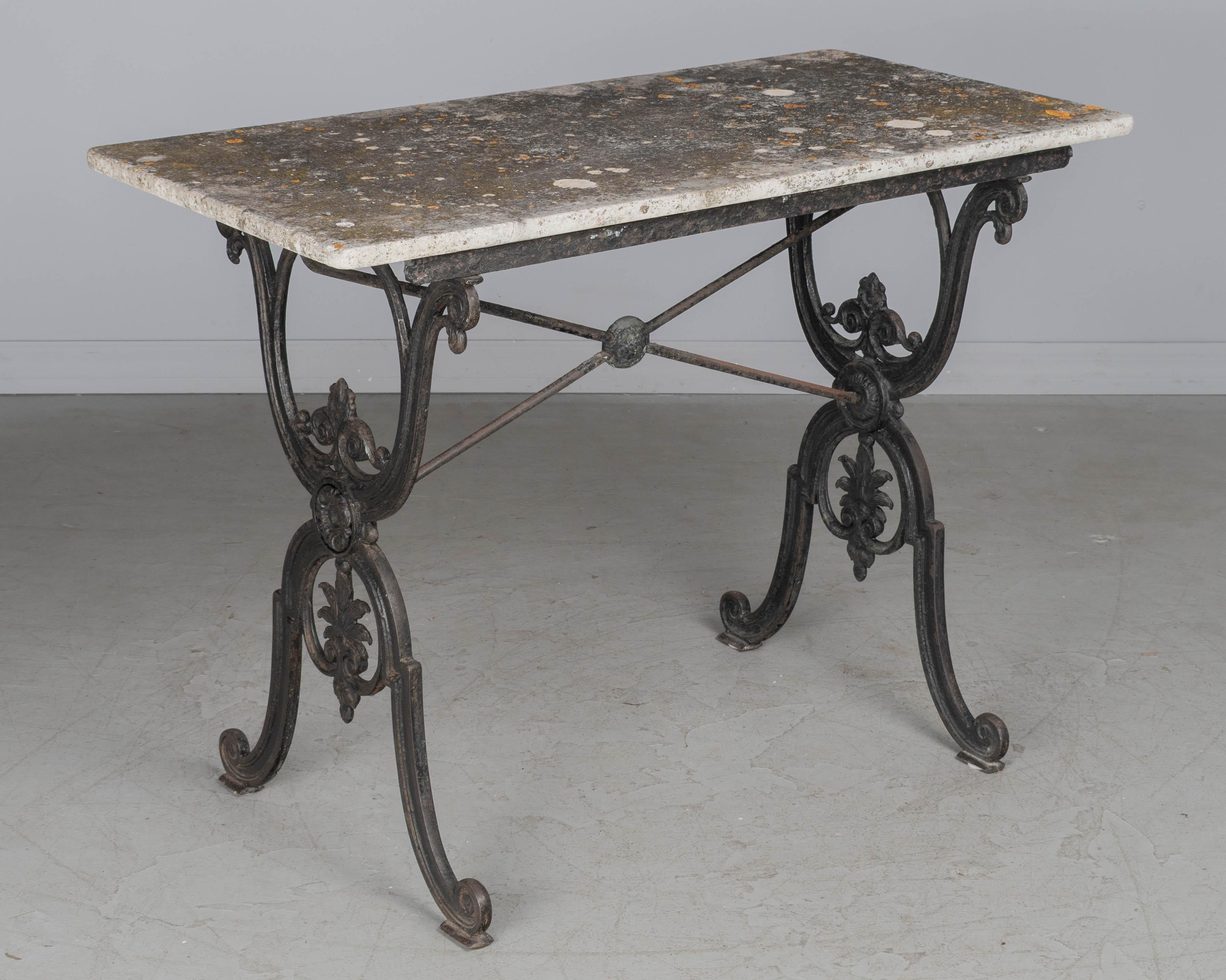 A 19th century French cast iron bistro table with black painted patina. Good heavy casting with elaborately detailed design. Marble has beautiful weathered surface with lichen and moss, hairline cracks. Marble is not original to the base but fits
