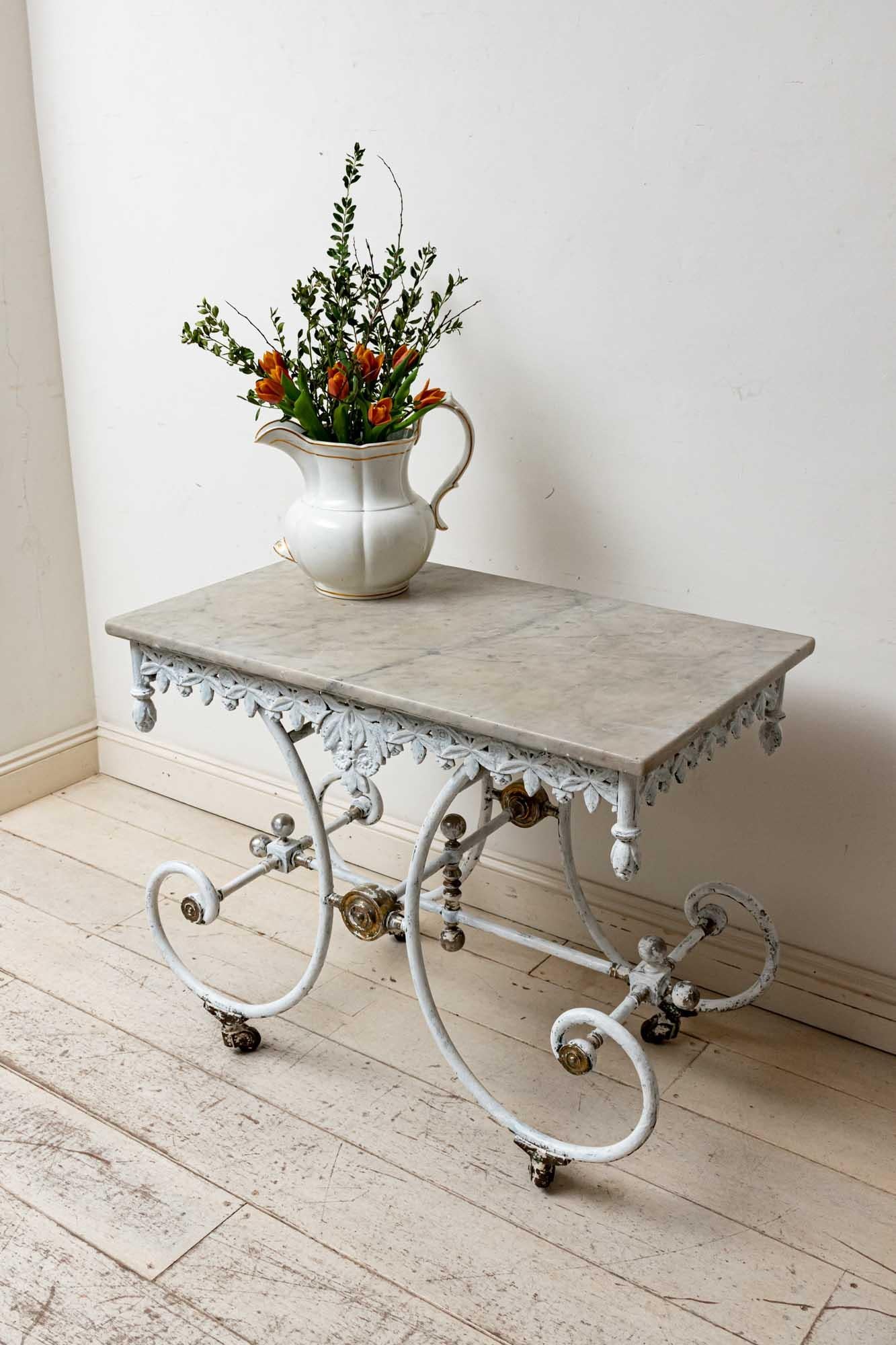 19th century French cast iron decorative patisserie table with the original marble top. The table features an unusual decorative frieze of leaves with a scrolled base, brass finials and medallions. The paint has been caringly refreshed and is